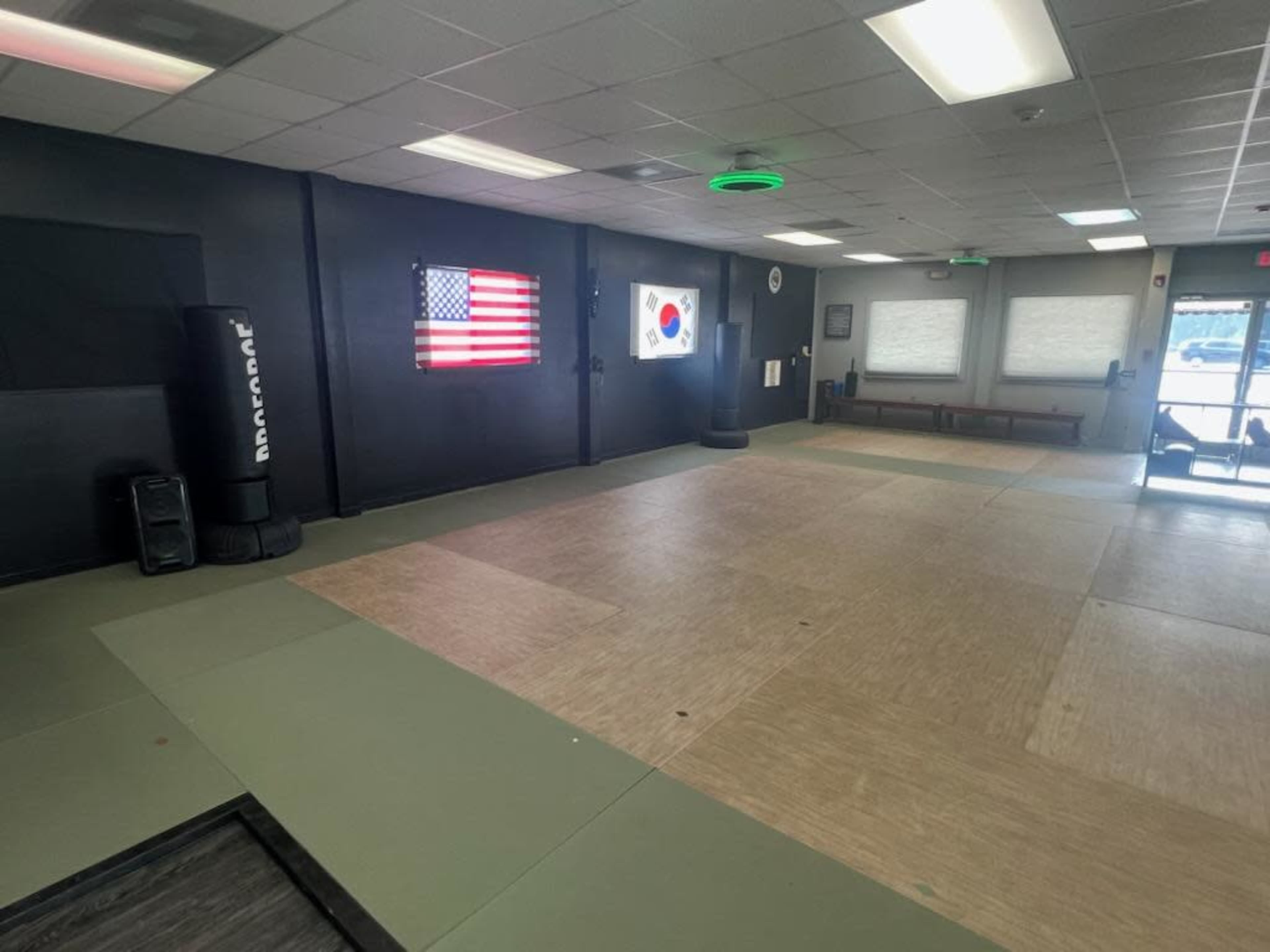 An empty martial arts training studio featuring an American flag and a South Korean flag mounted on the walls.