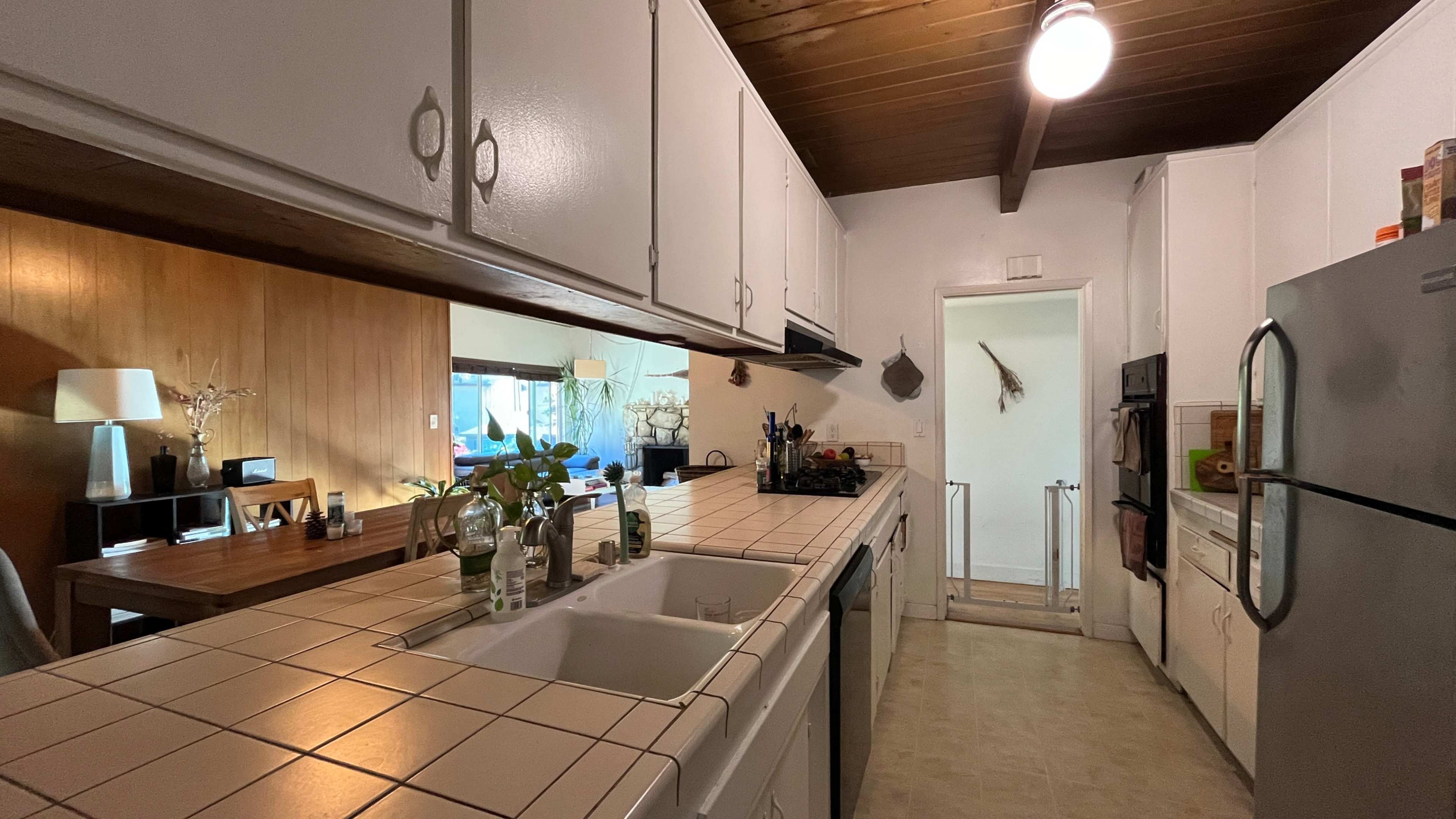 The kitchen features white cabinets, a tiled countertop, and appliances along one wall, with a small dining area visible in the background.