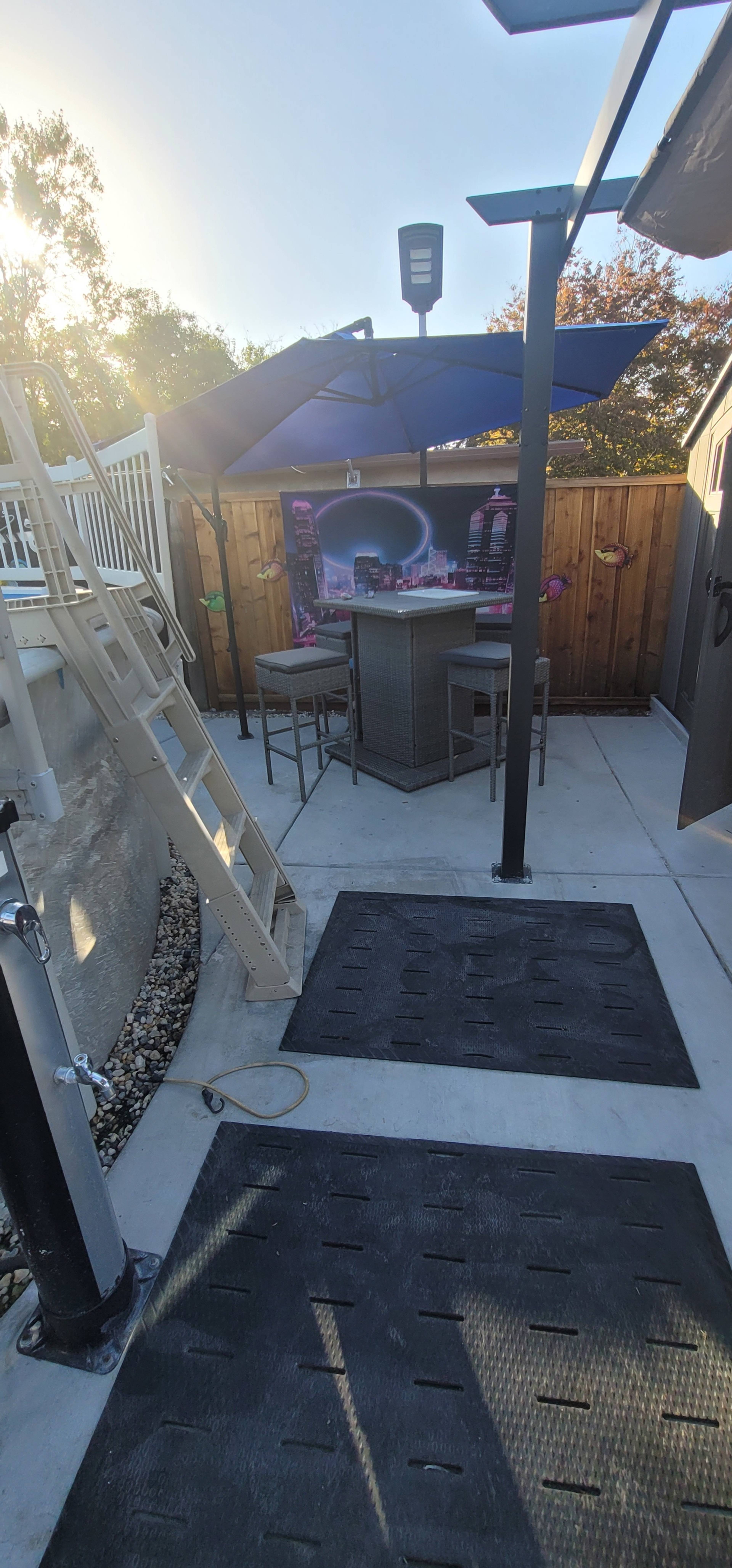 A patio area with a bar under an umbrella next to a swimming pool, featuring a ladder leading into the water.