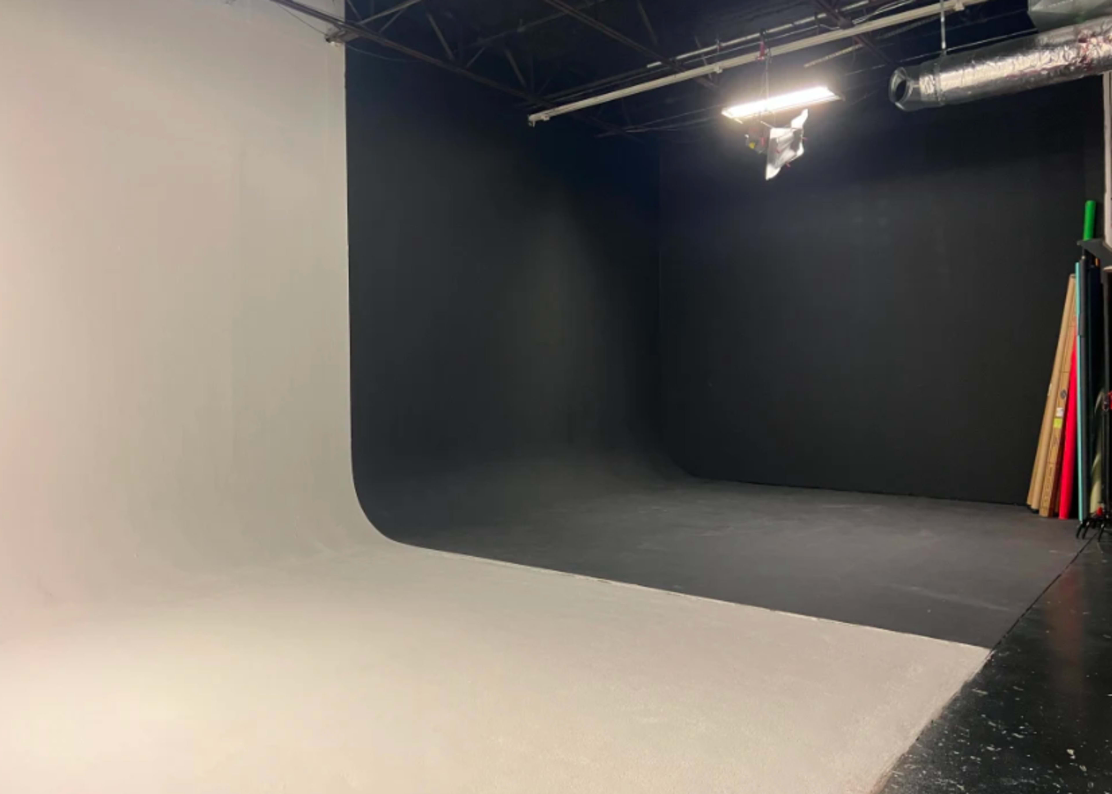 The image shows a photography studio with a large, curved white backdrop on one side and a dark black backdrop on the other.