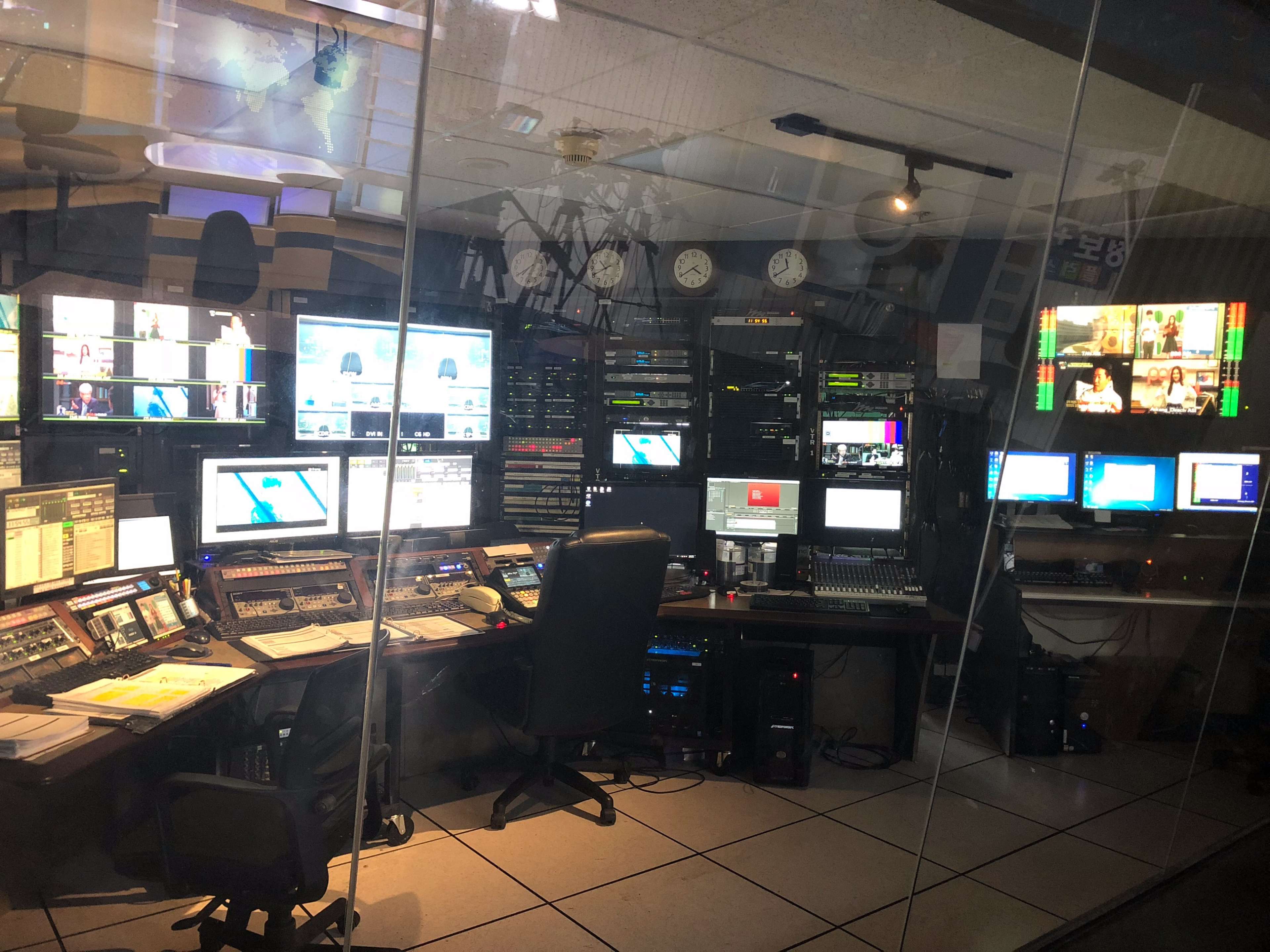 A television control room filled with various monitors, editing equipment, and soundboards, all housed within a glass enclosure.