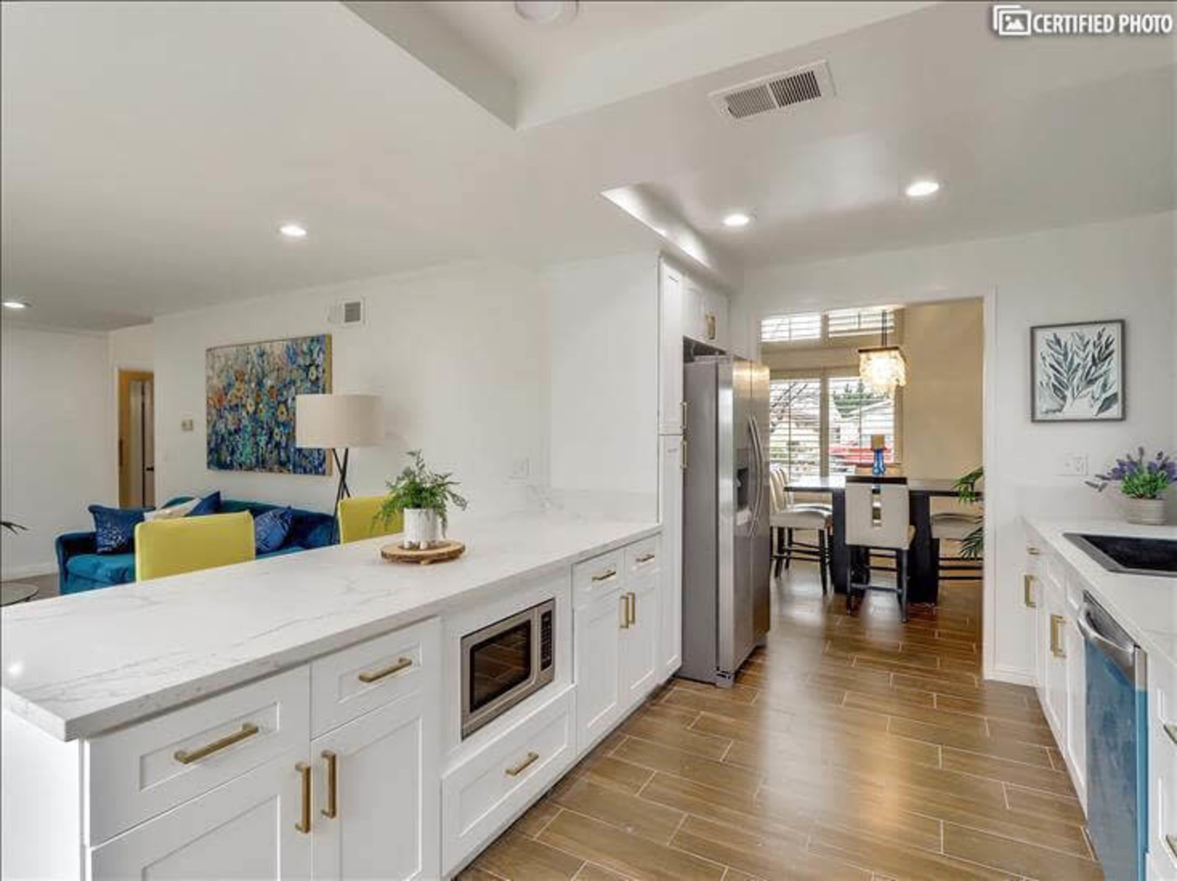 A modern kitchen with white cabinetry, a stainless steel refrigerator, and a dining area visible through an open doorway.