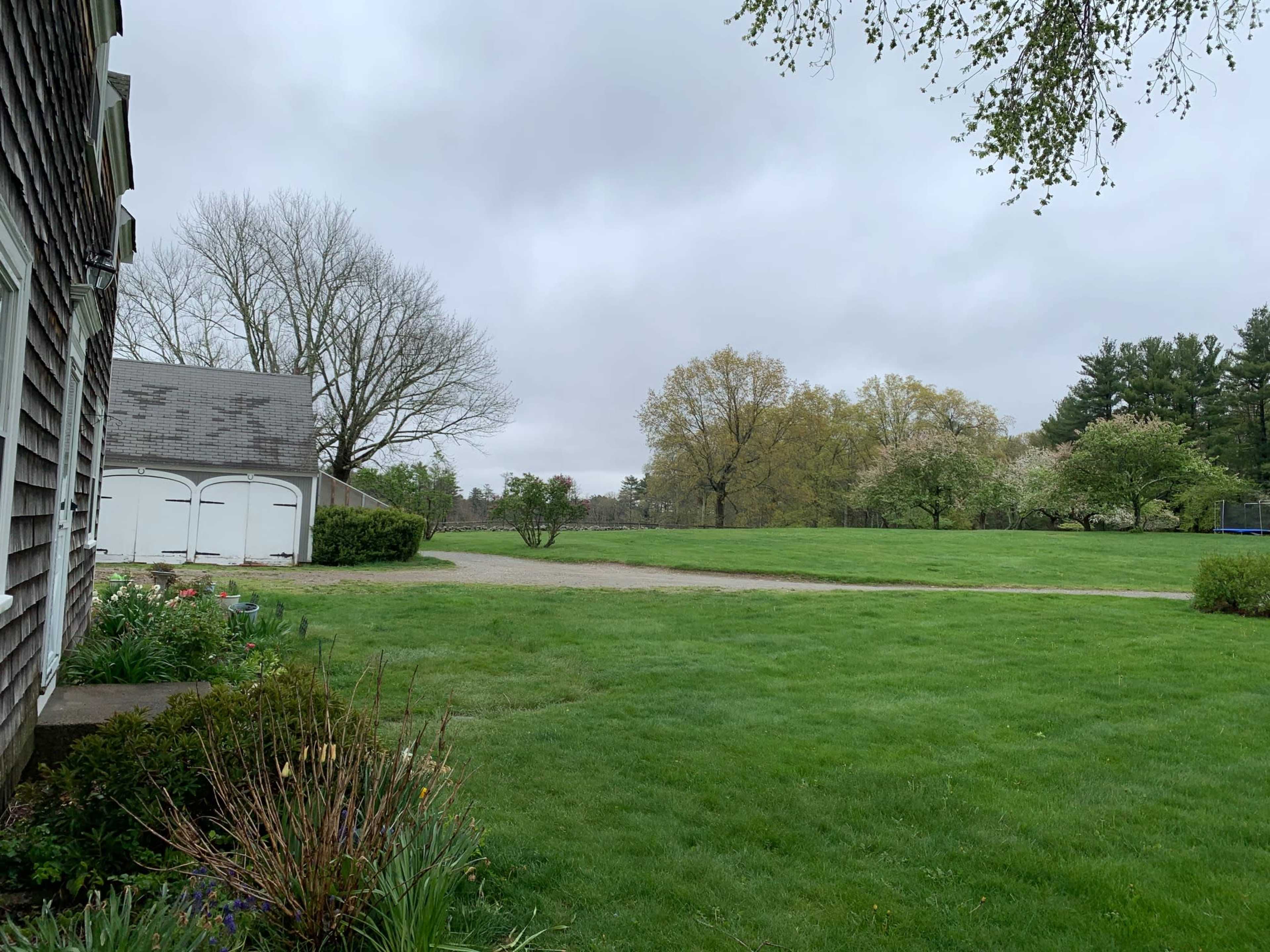 A grassy yard is shown, bordered by a house and a garage, under a cloudy sky with trees in the background.