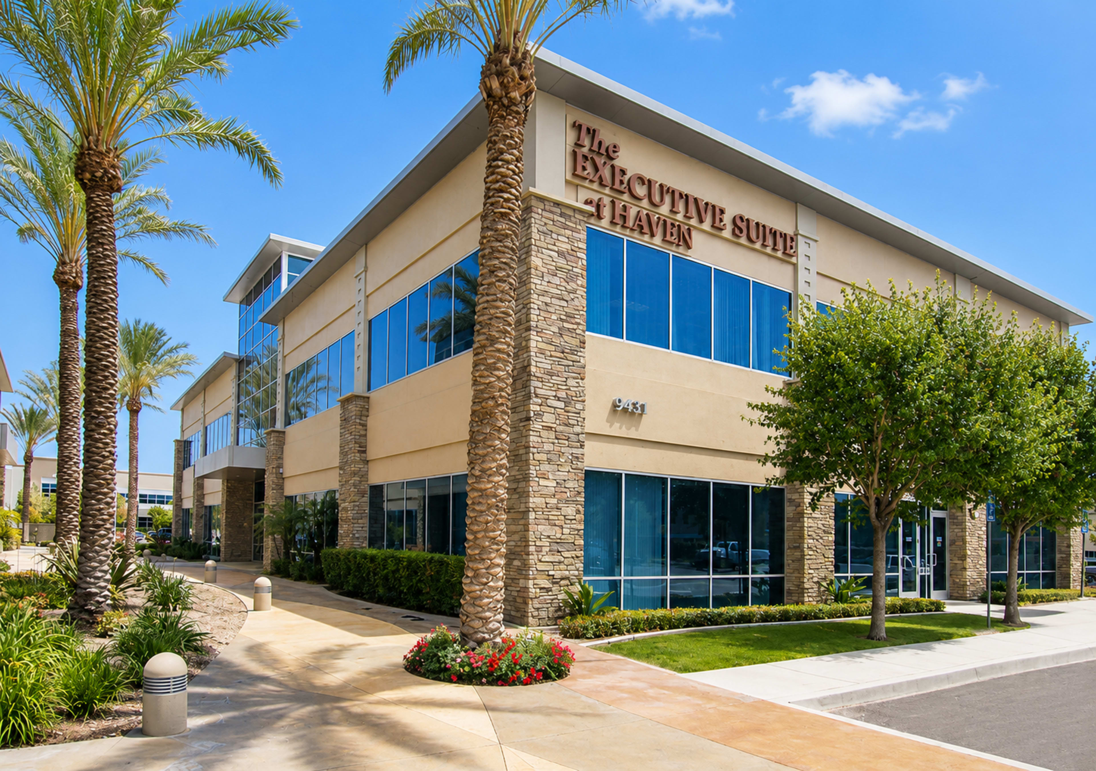 The image shows a modern, two-story office building with large windows, surrounded by palm trees and landscaped greenery.