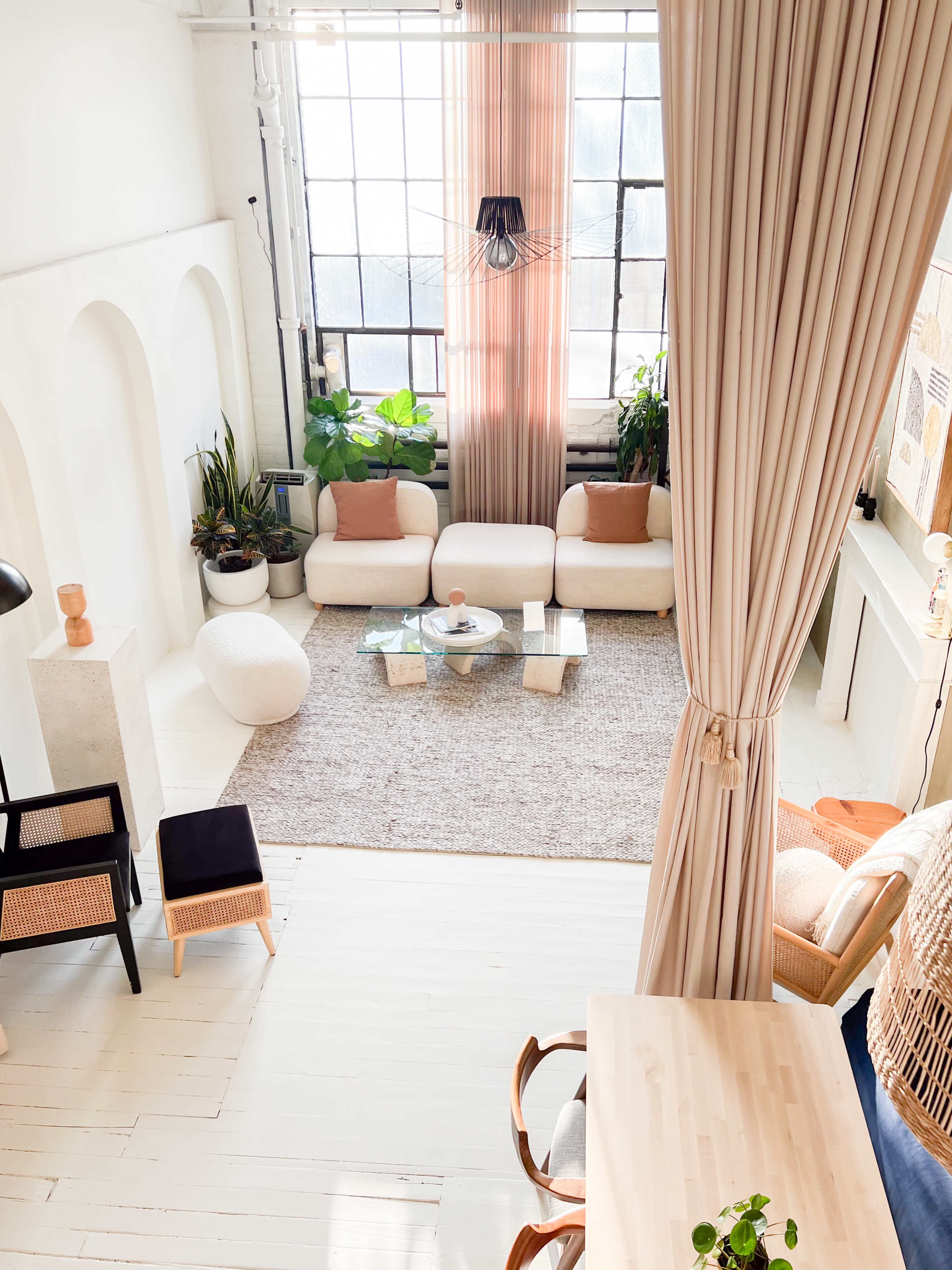 A bright, airy living space with large windows, a neutral color palette, modern furniture, and various plants.