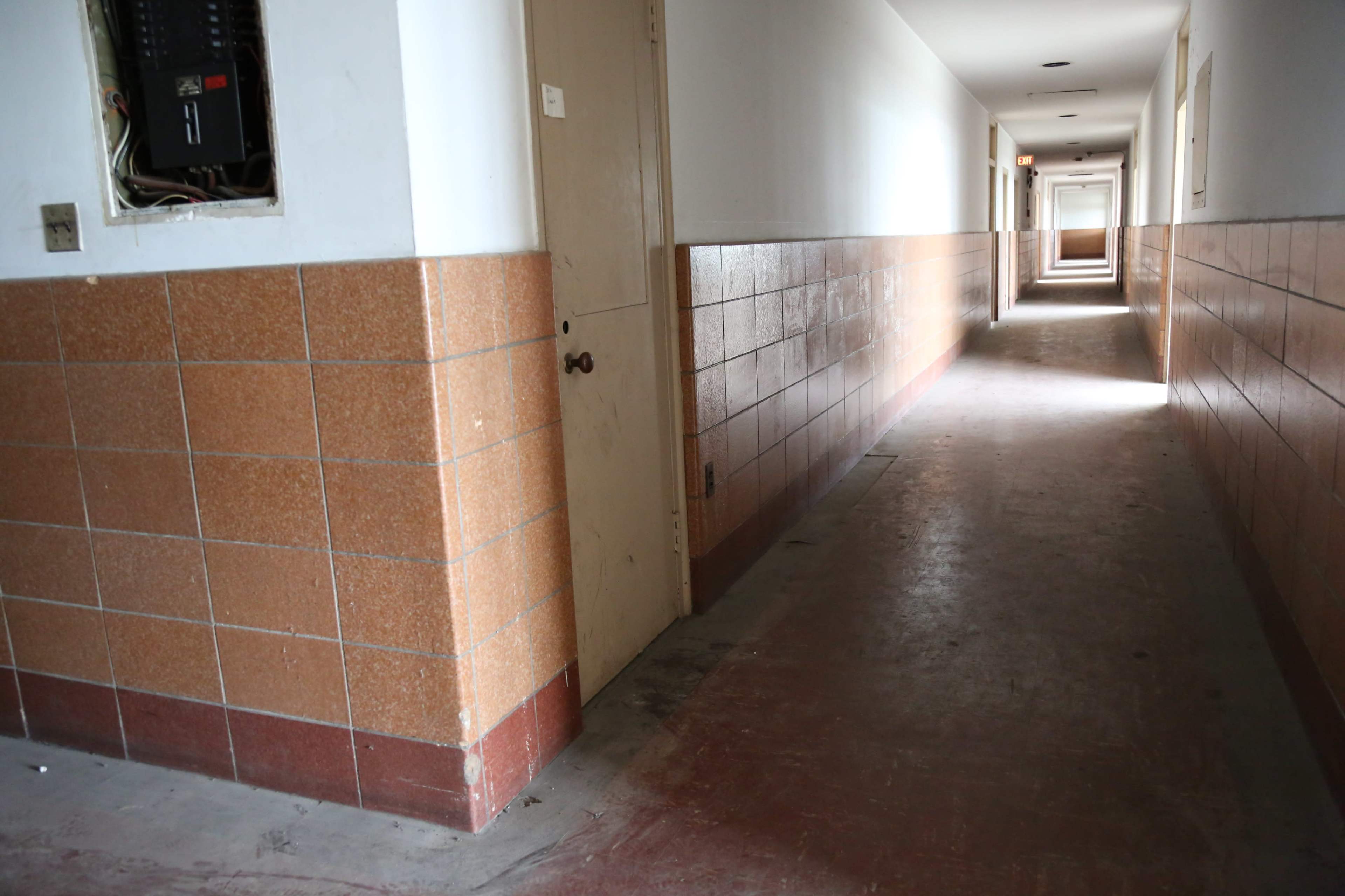 A long, narrow hallway with tiled walls and a doorway leading to another room.