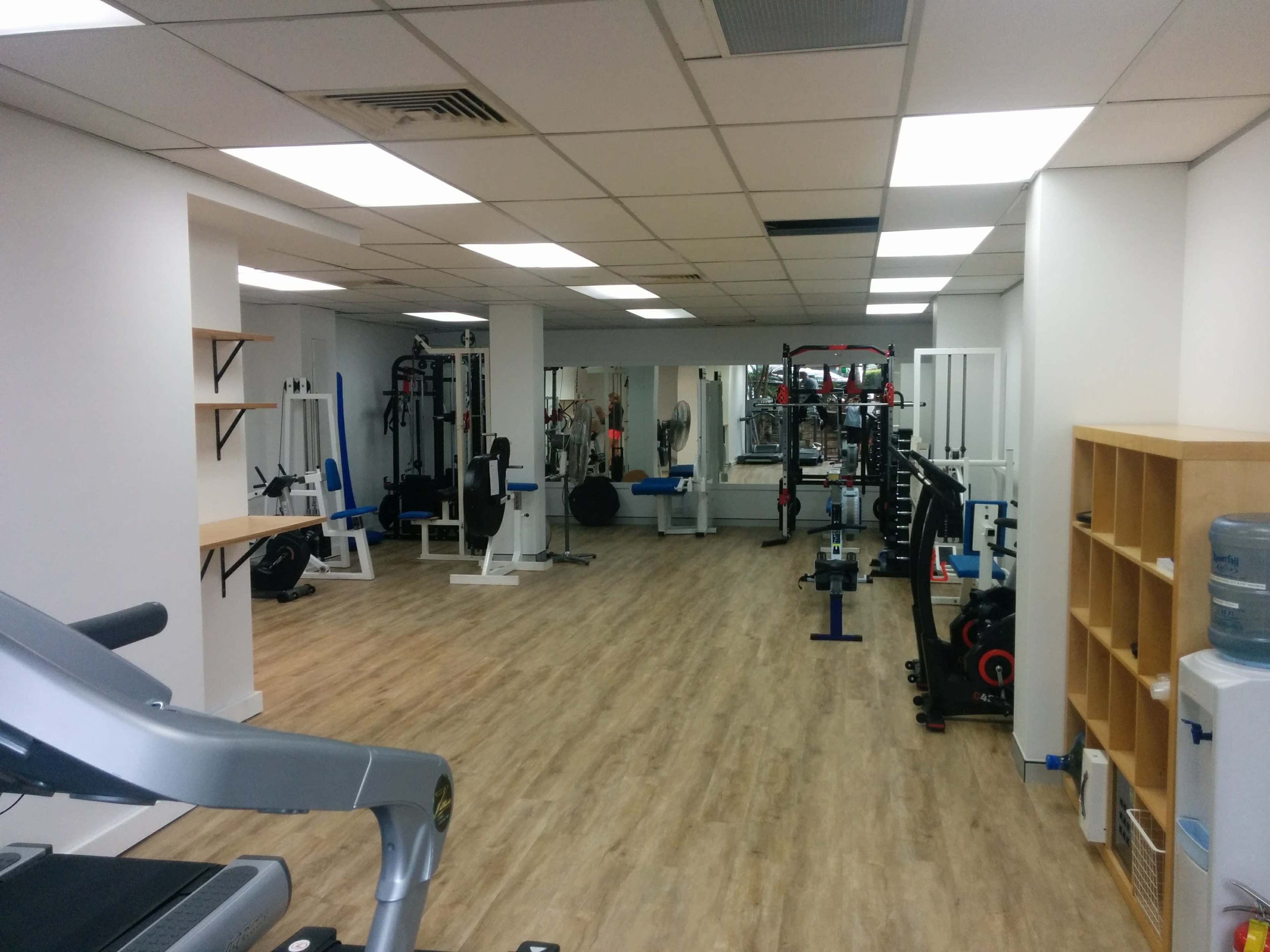The image shows a spacious gym with various exercise equipment, including weightlifting stations, cardio machines, and open floor space.