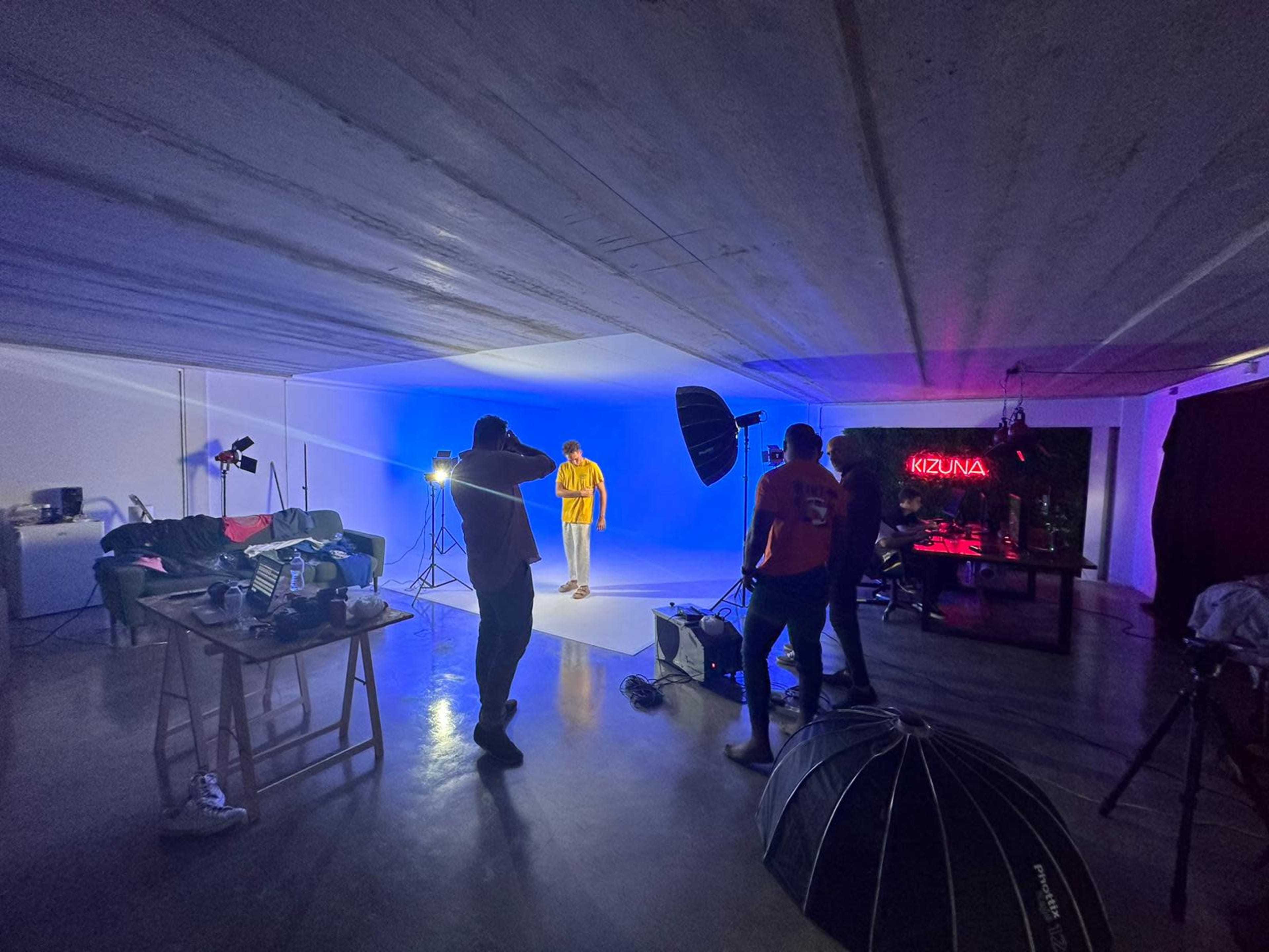 A group of individuals is setting up lighting equipment in a studio with a blue backdrop to facilitate a photoshoot.