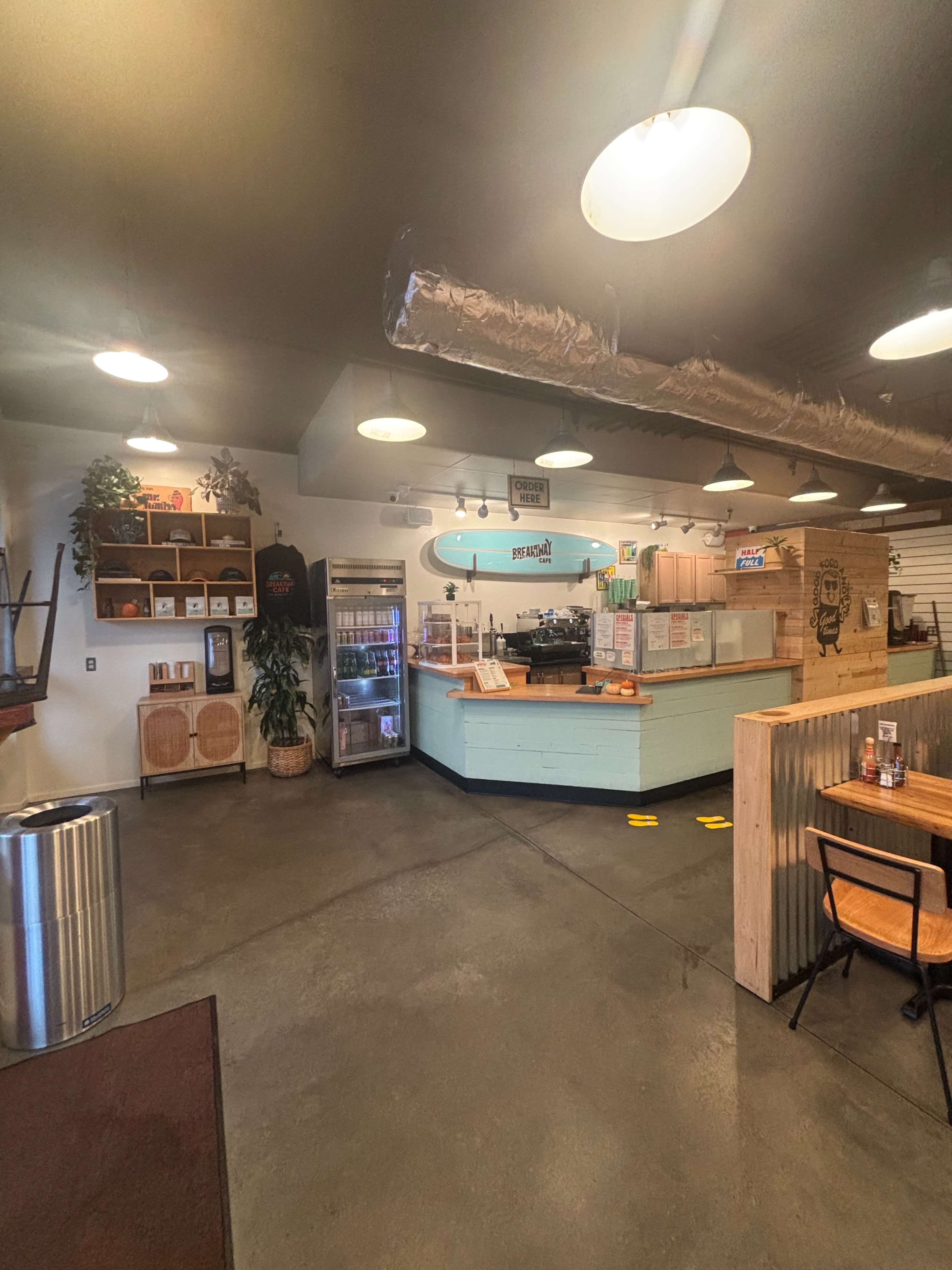 The image shows a modern cafe interior with a service counter, seating area, and decorative plants.