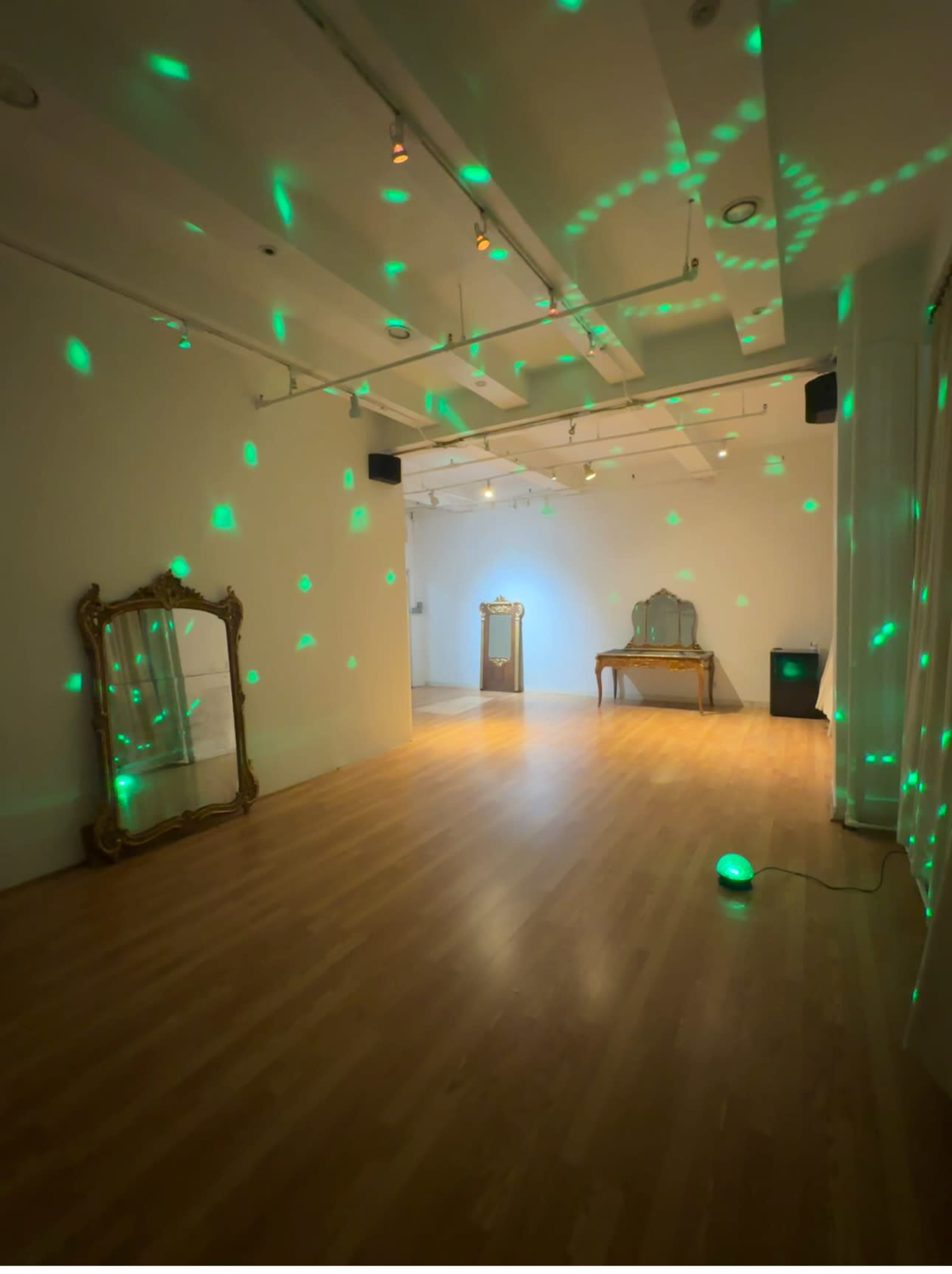 The image shows a spacious, well-lit room featuring wooden flooring, decorative mirrors, and green light dots projected on the walls and ceiling.