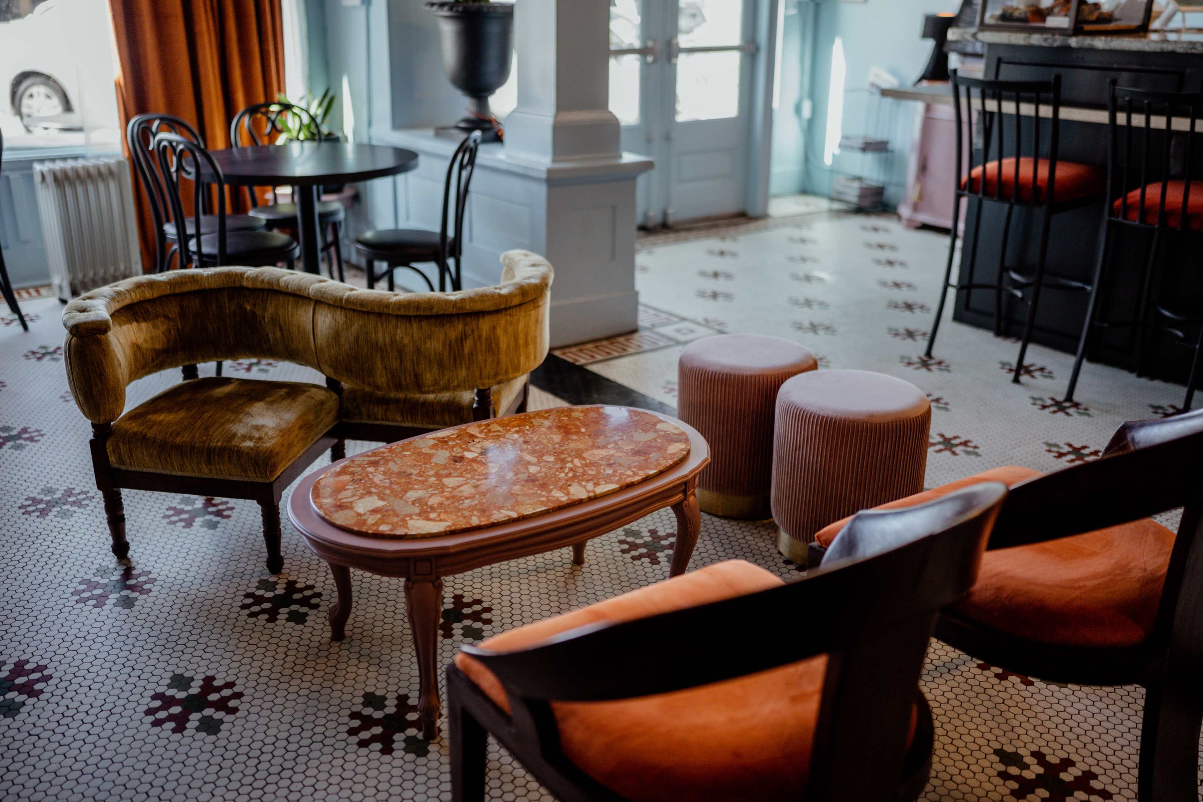 A stylish seating area features a curved velvet sofa, a marble coffee table, and upholstered chairs on a patterned tile floor.
