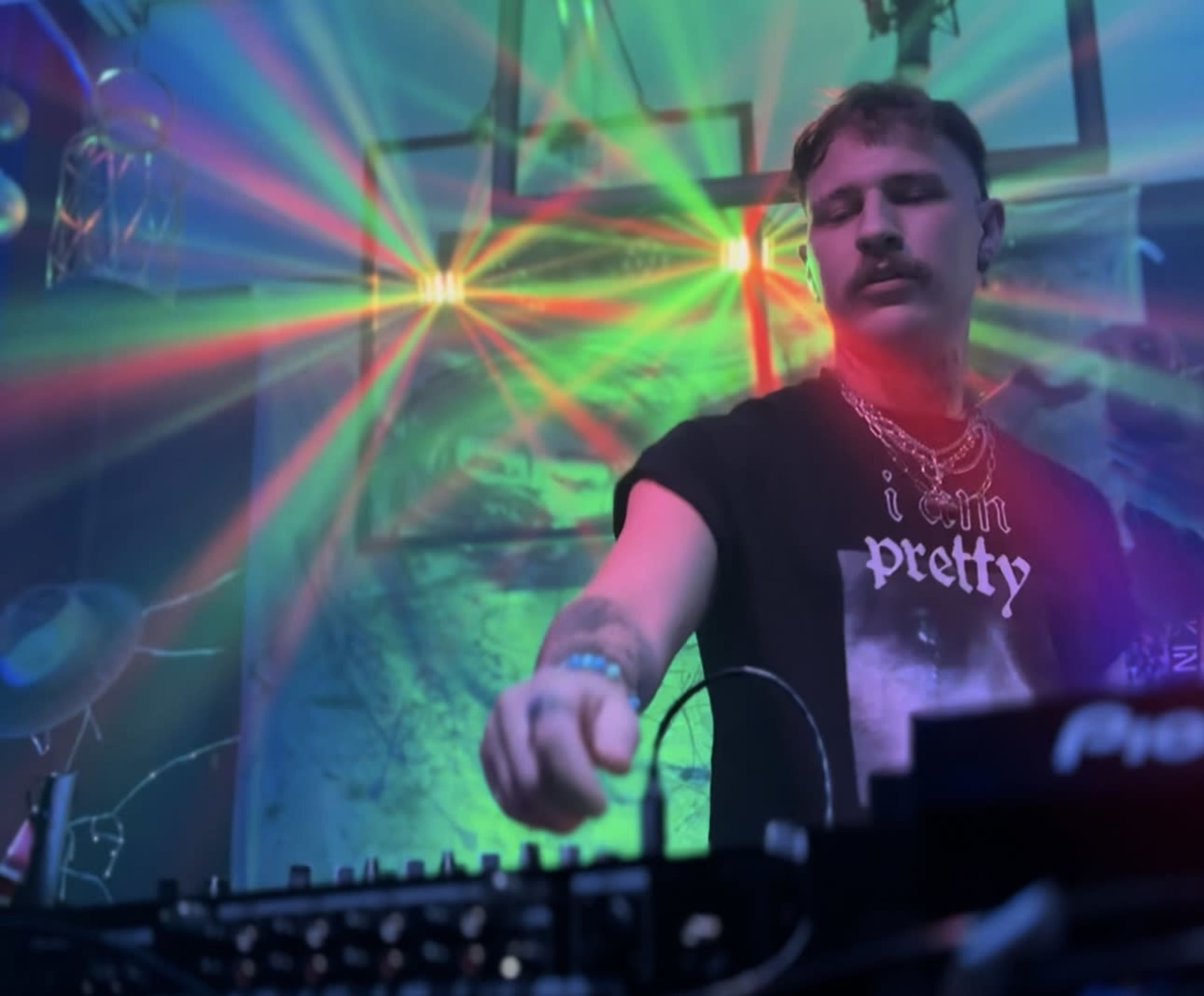 A DJ performs at a colorful light-lit venue, surrounded by vibrant beams of light.