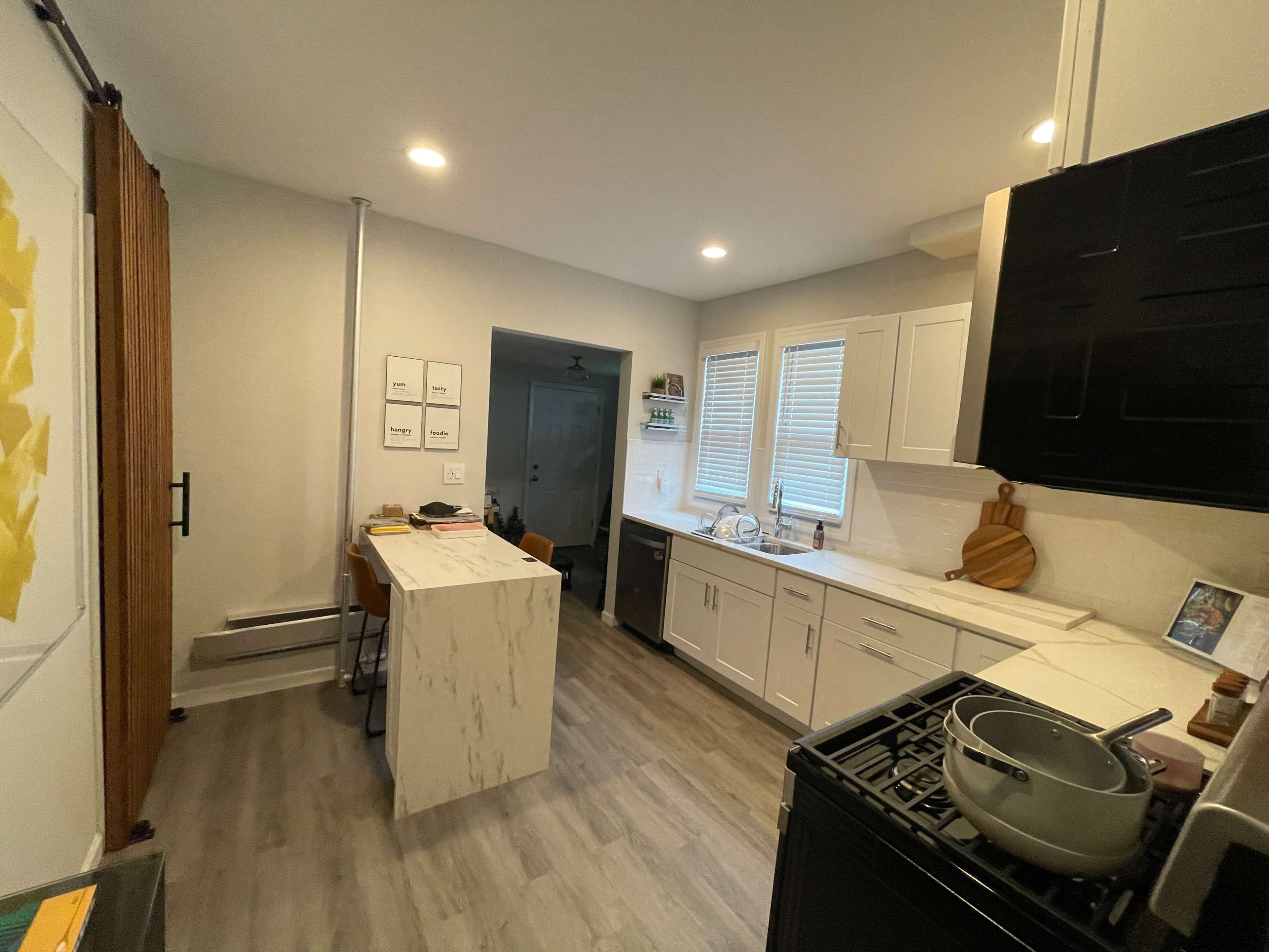 A modern kitchen featuring a central island with a marble surface, white cabinetry, and a window that provides natural light.
