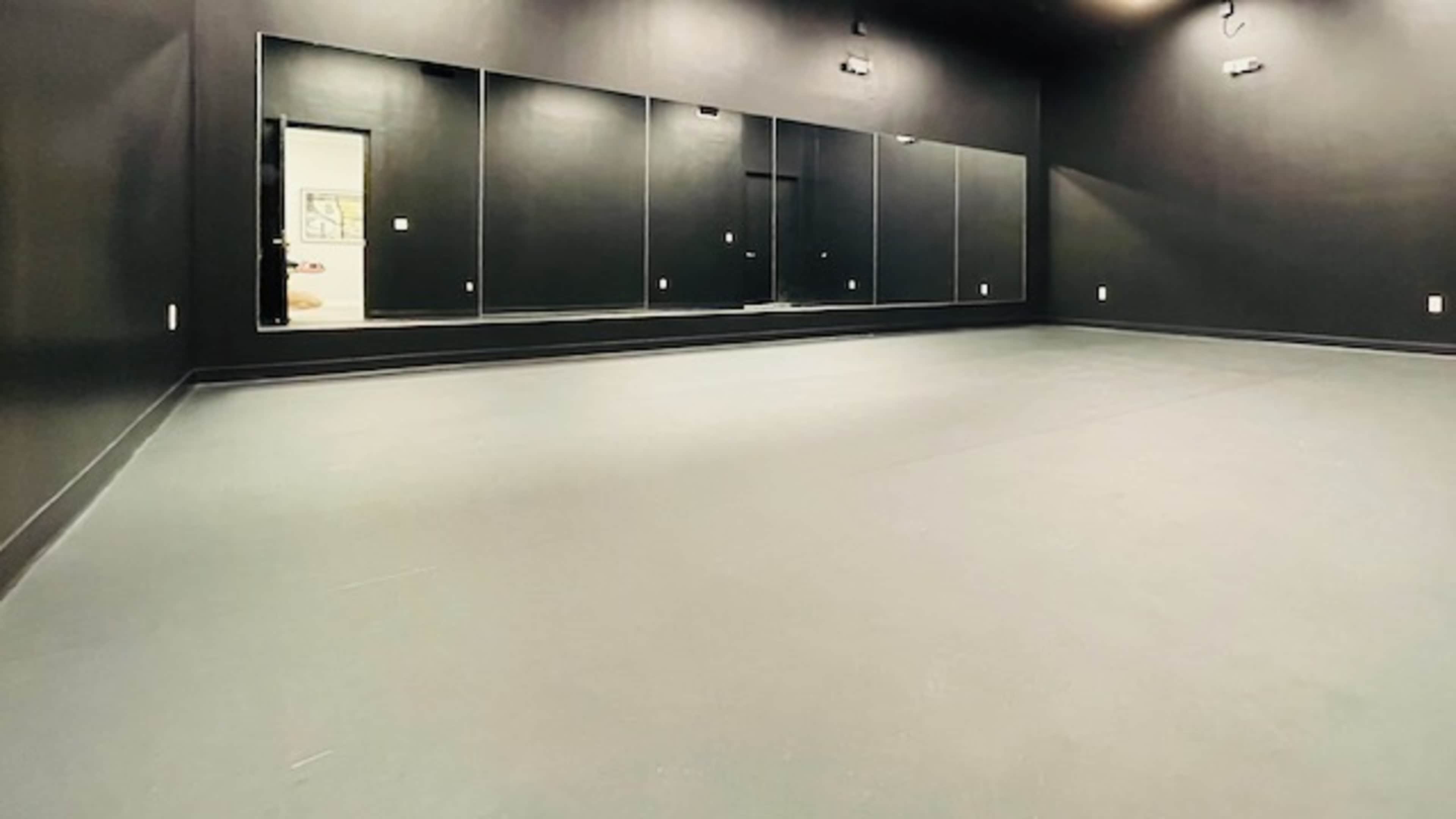 A spacious room with black walls, a mirrored wall, and a grey floor.