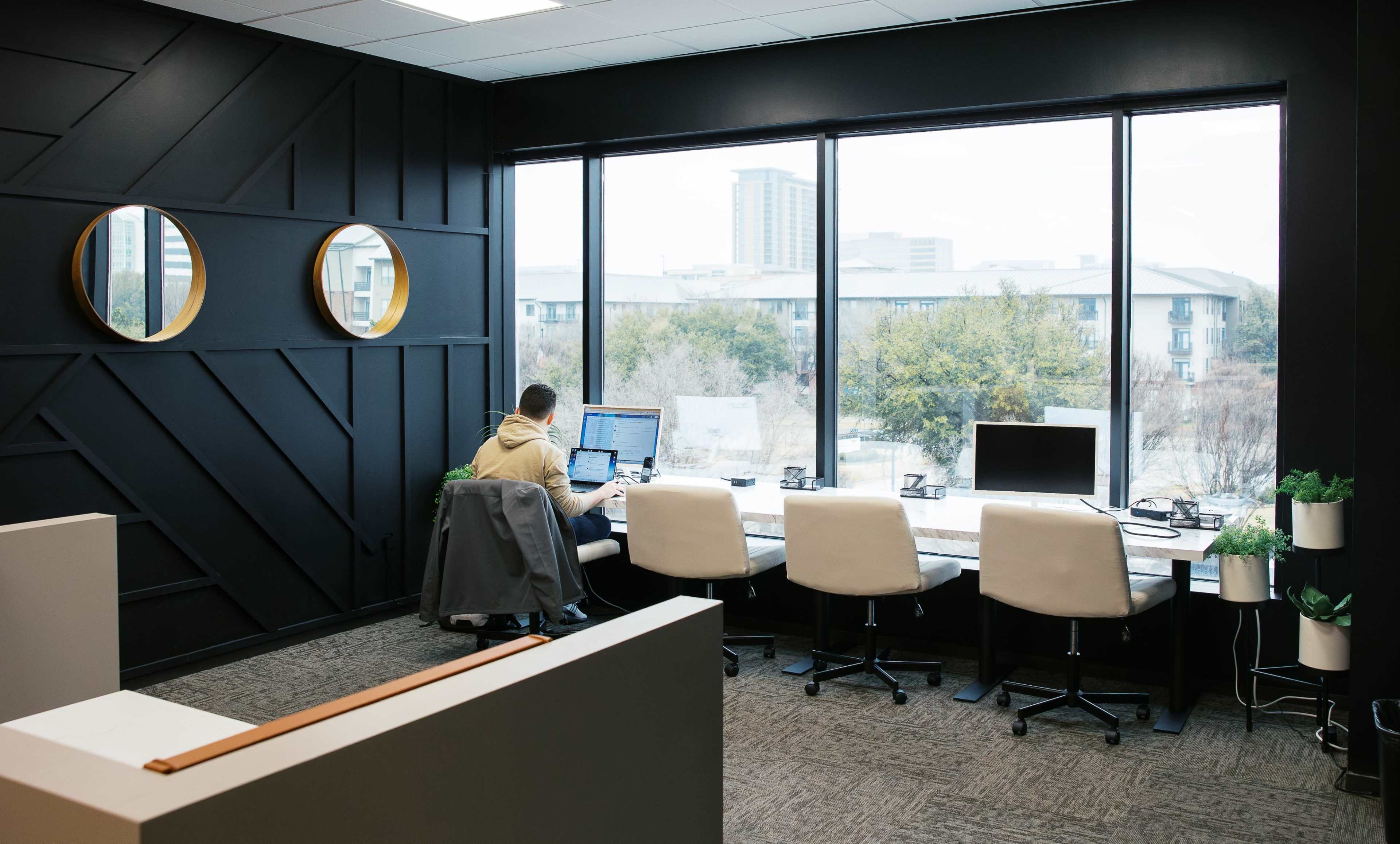 A person works at a desk in a modern office with large windows that overlook a cityscape.