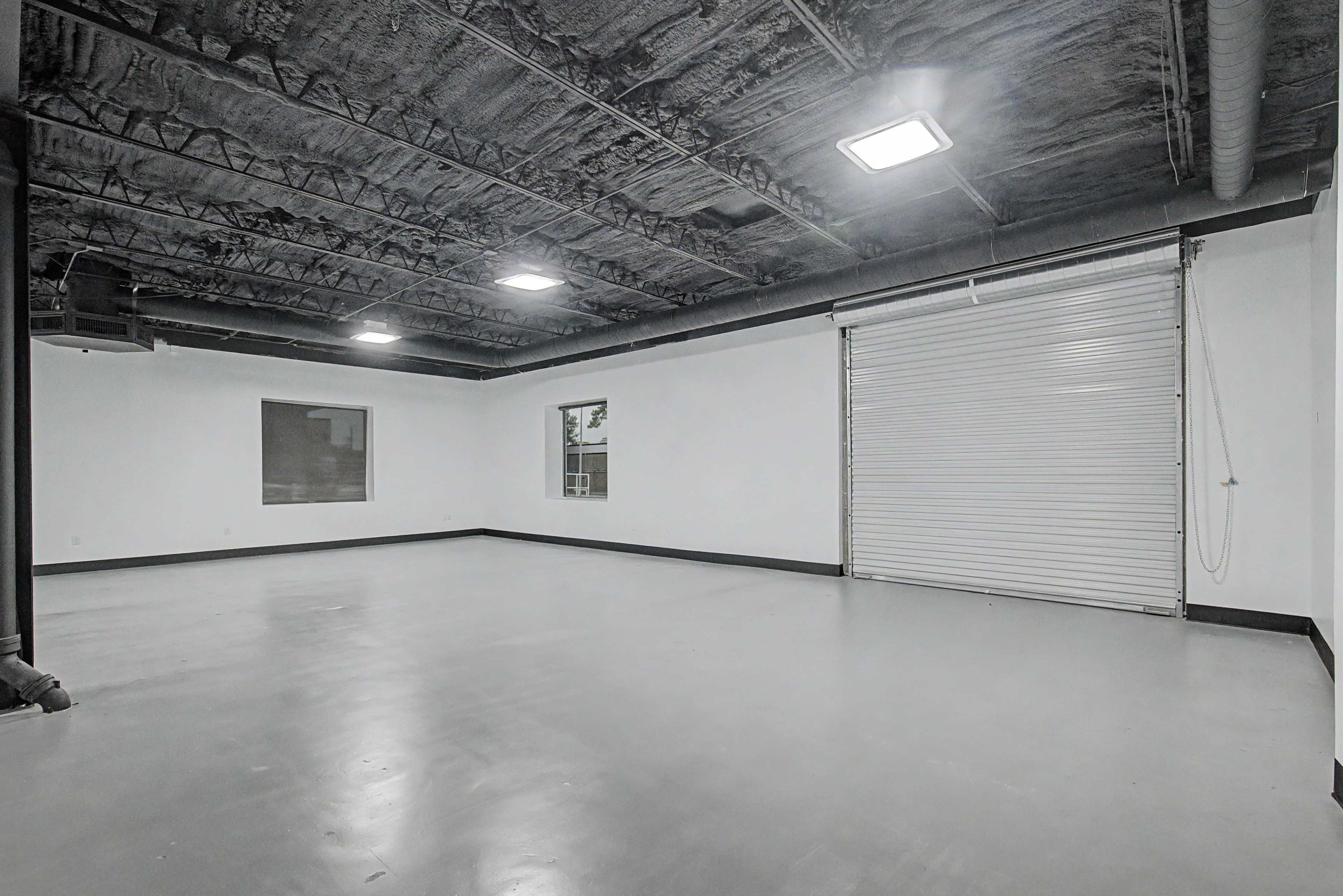 The image shows an empty, industrial-style room with a flat floor, gray walls, and a large roll-up door.