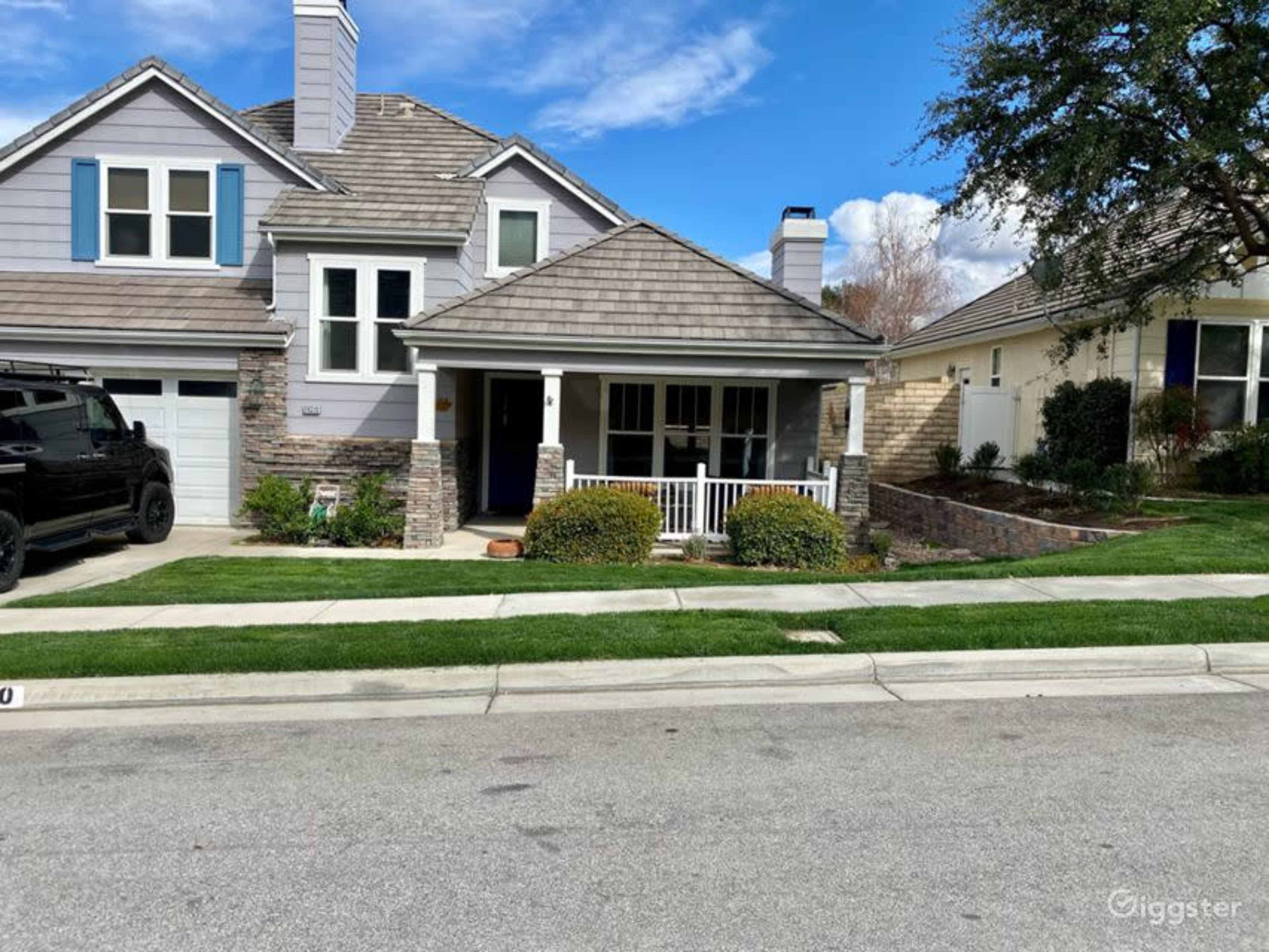 A suburban house with a stone and siding exterior features a covered front porch and a manicured lawn, situated on a quiet street.