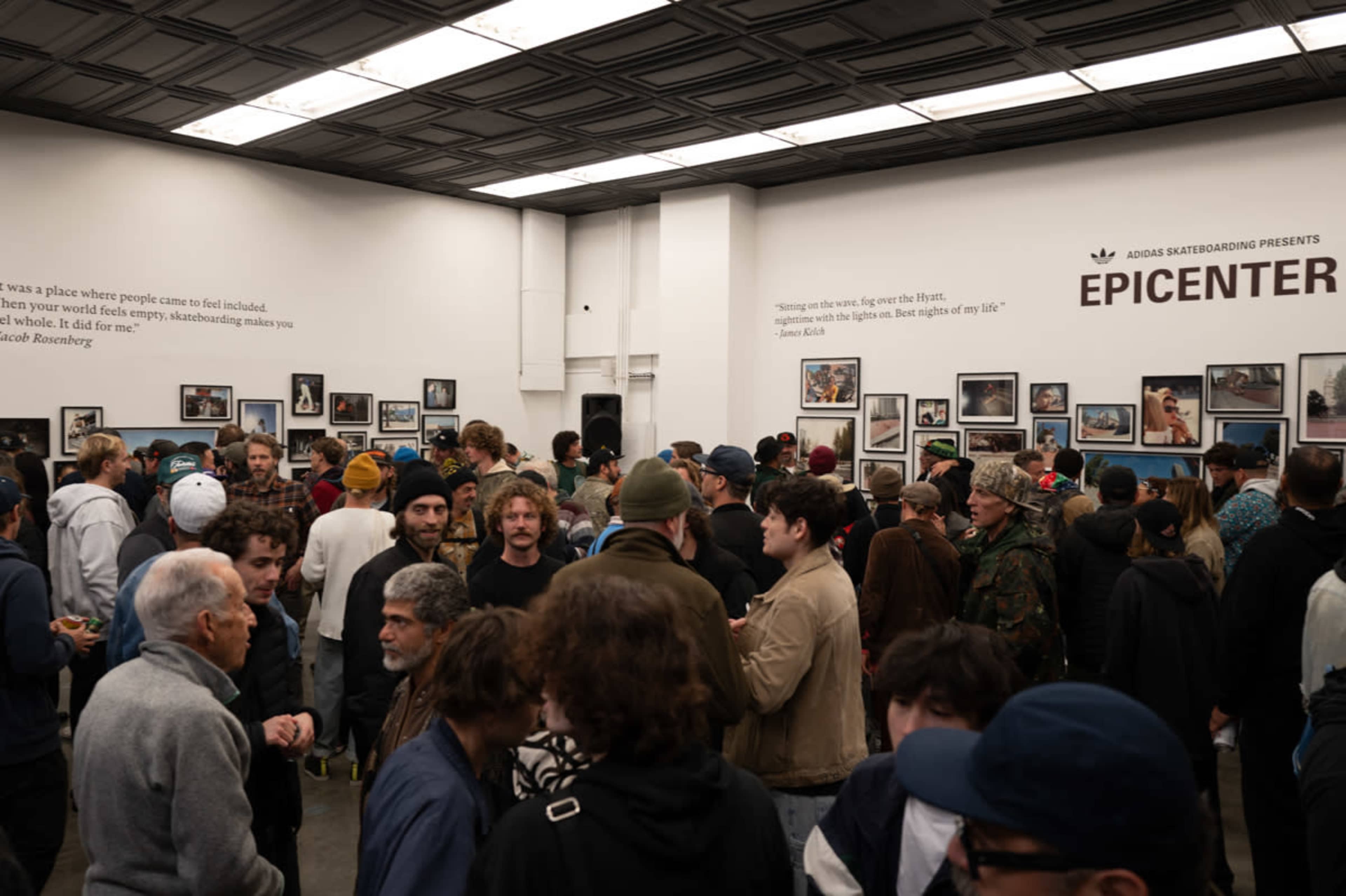 A large crowd gathers in an art gallery, socializing around framed photographs displayed on the walls.