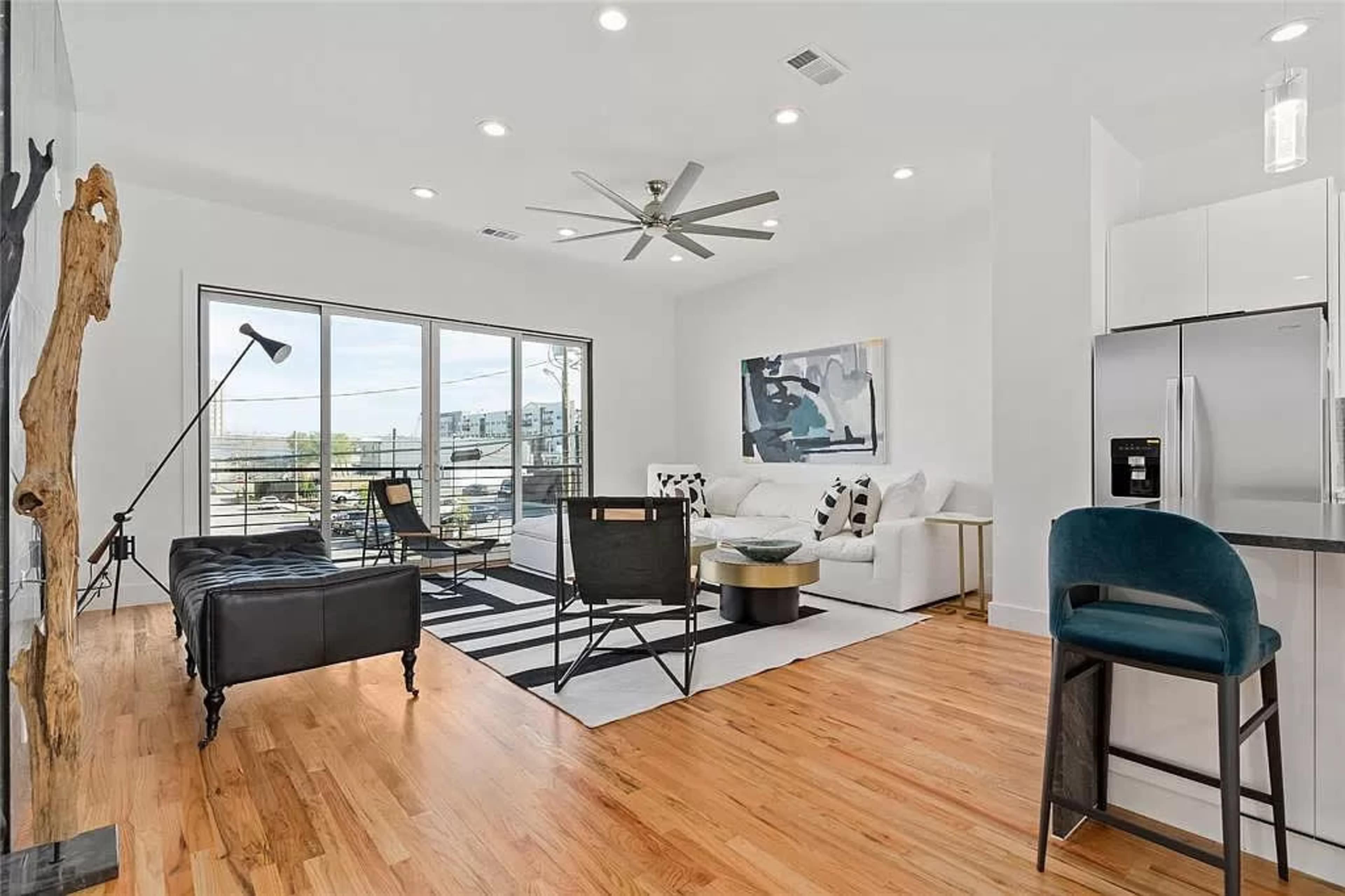 A modern living room featuring a black leather sofa, white armchairs, a round coffee table, and large windows allowing natural light to fill the space.