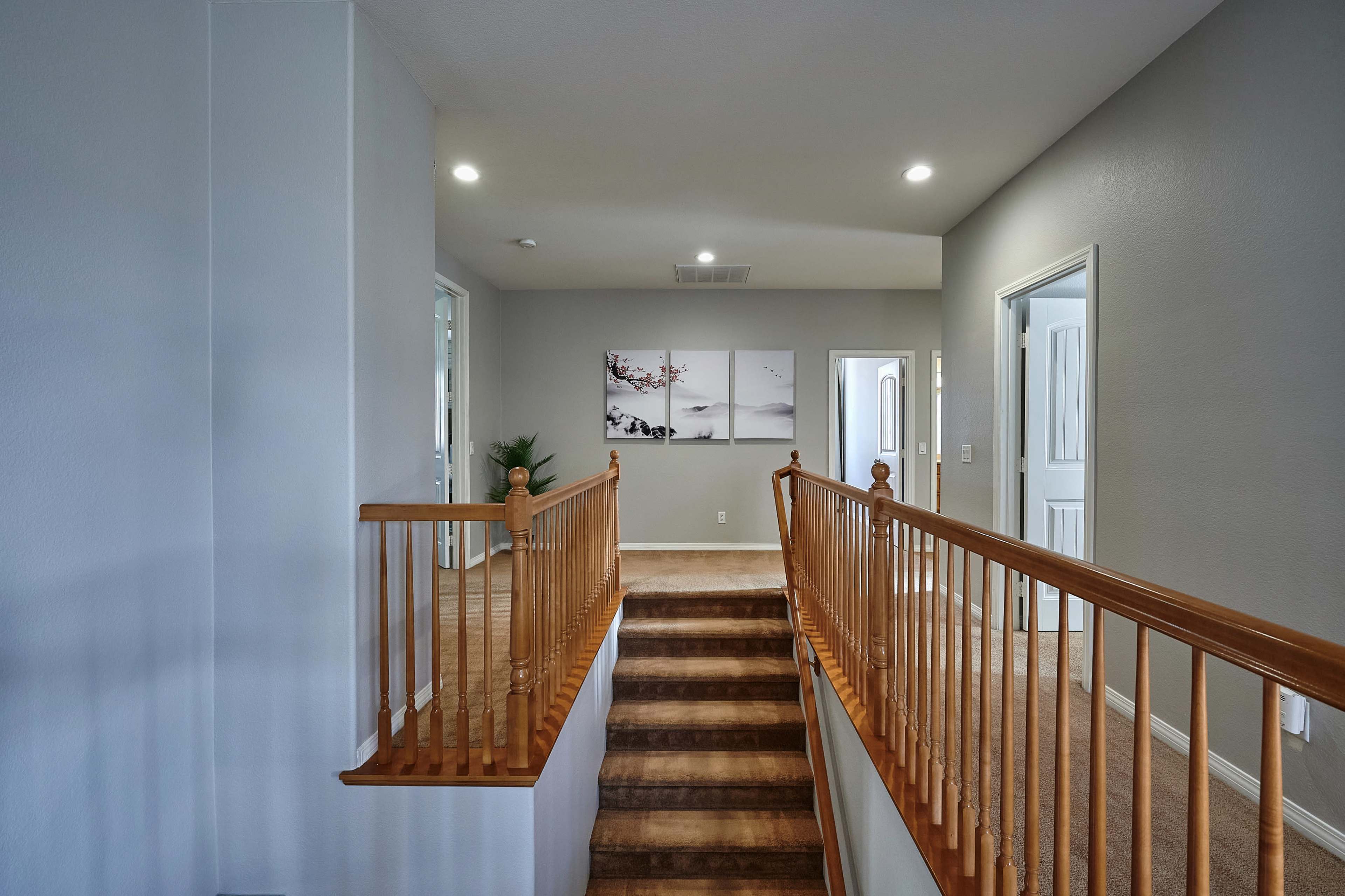 A carpeted hallway with a wooden banister, leading to multiple doorways and a bright wall art feature.