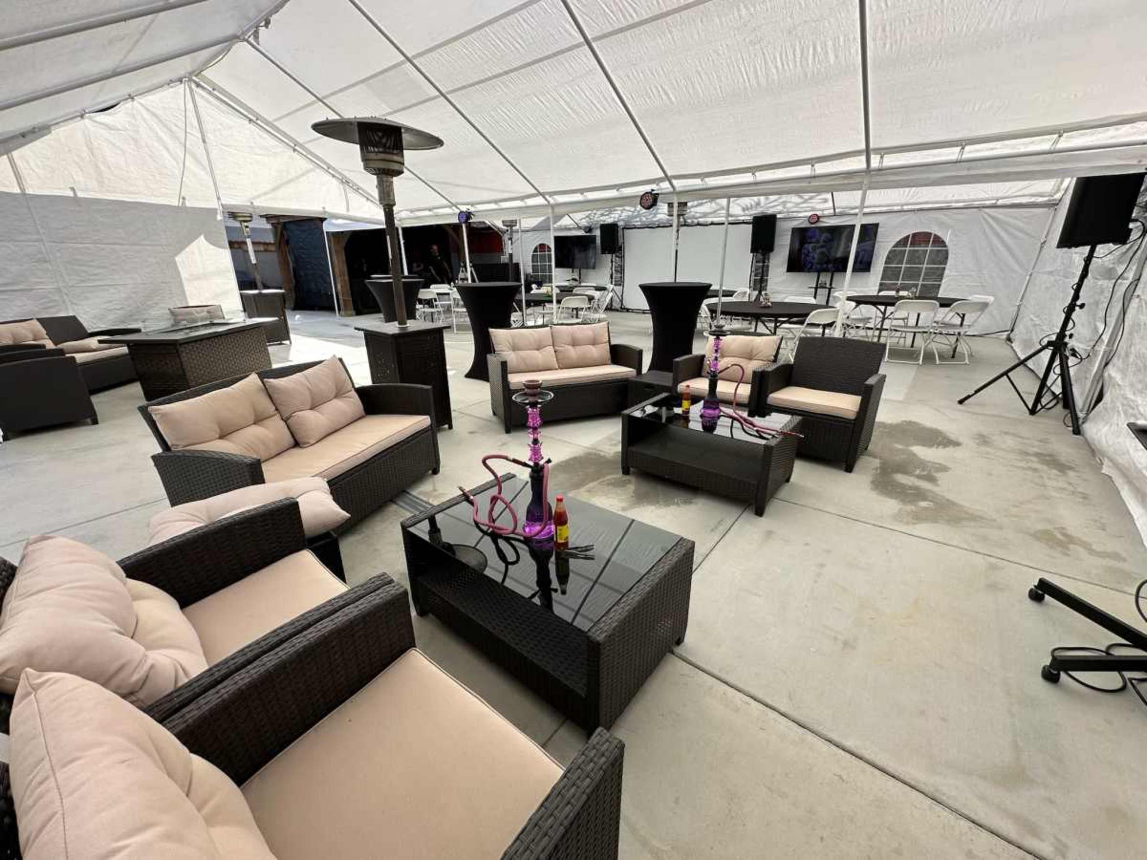 The image shows a spacious, white tent featuring several seating areas with wicker furniture, tables, and a hookah setup.