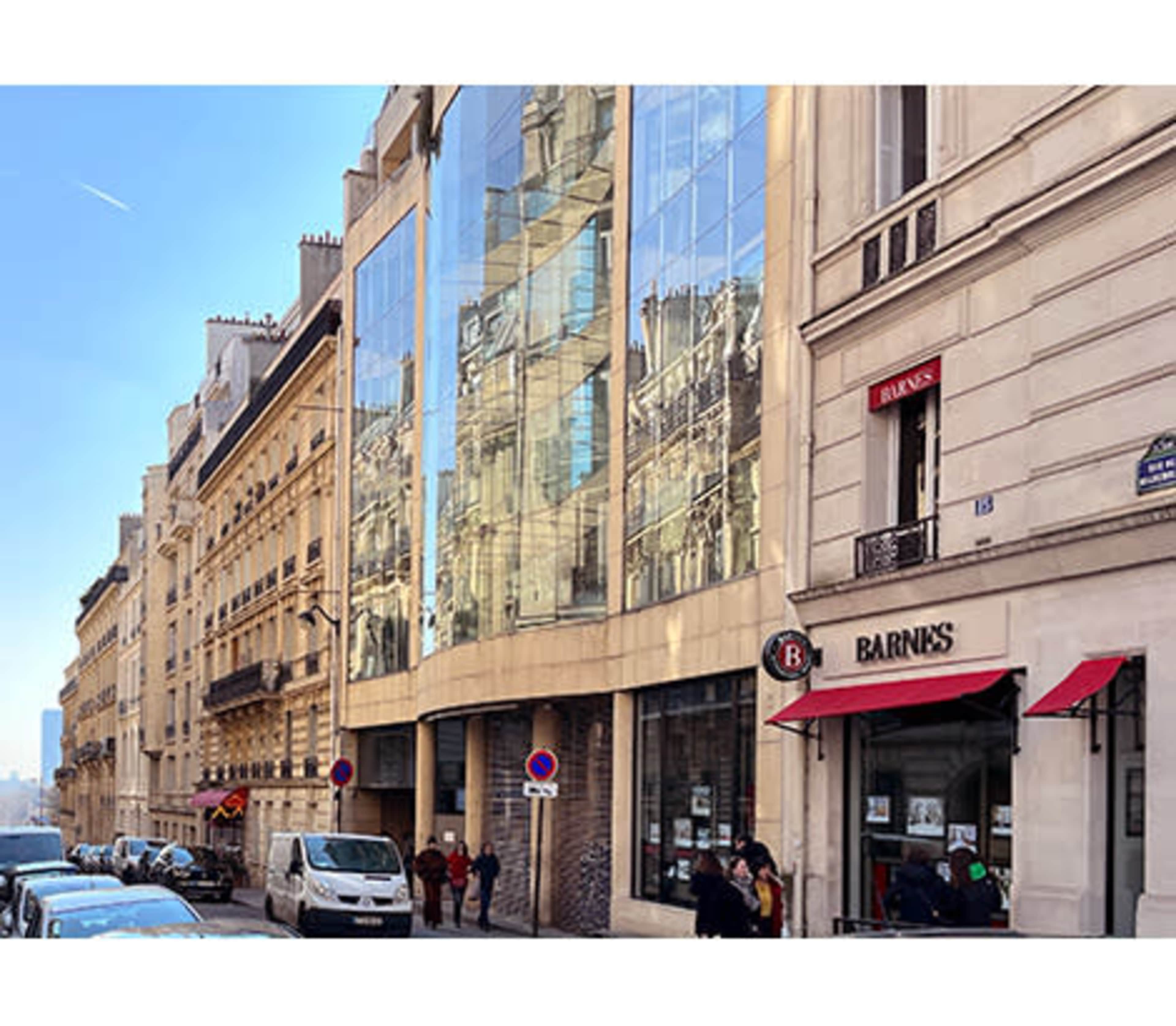 A street in Paris showcasing a mix of traditional and modern architecture, with reflective glass facades alongside classic stone buildings.
