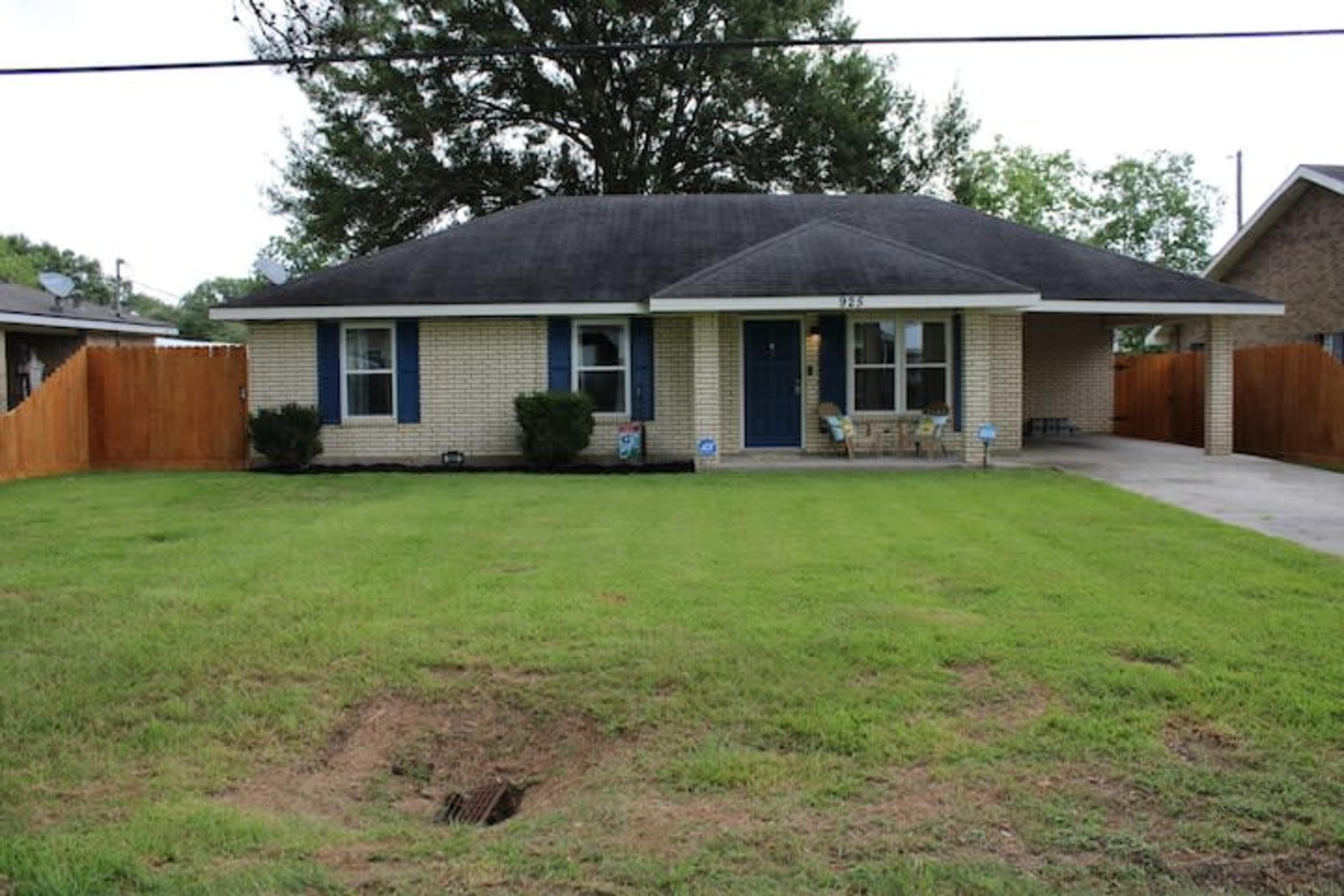 The image shows a single-story brick house with a neatly maintained lawn and a wooden fence surrounding the yard.