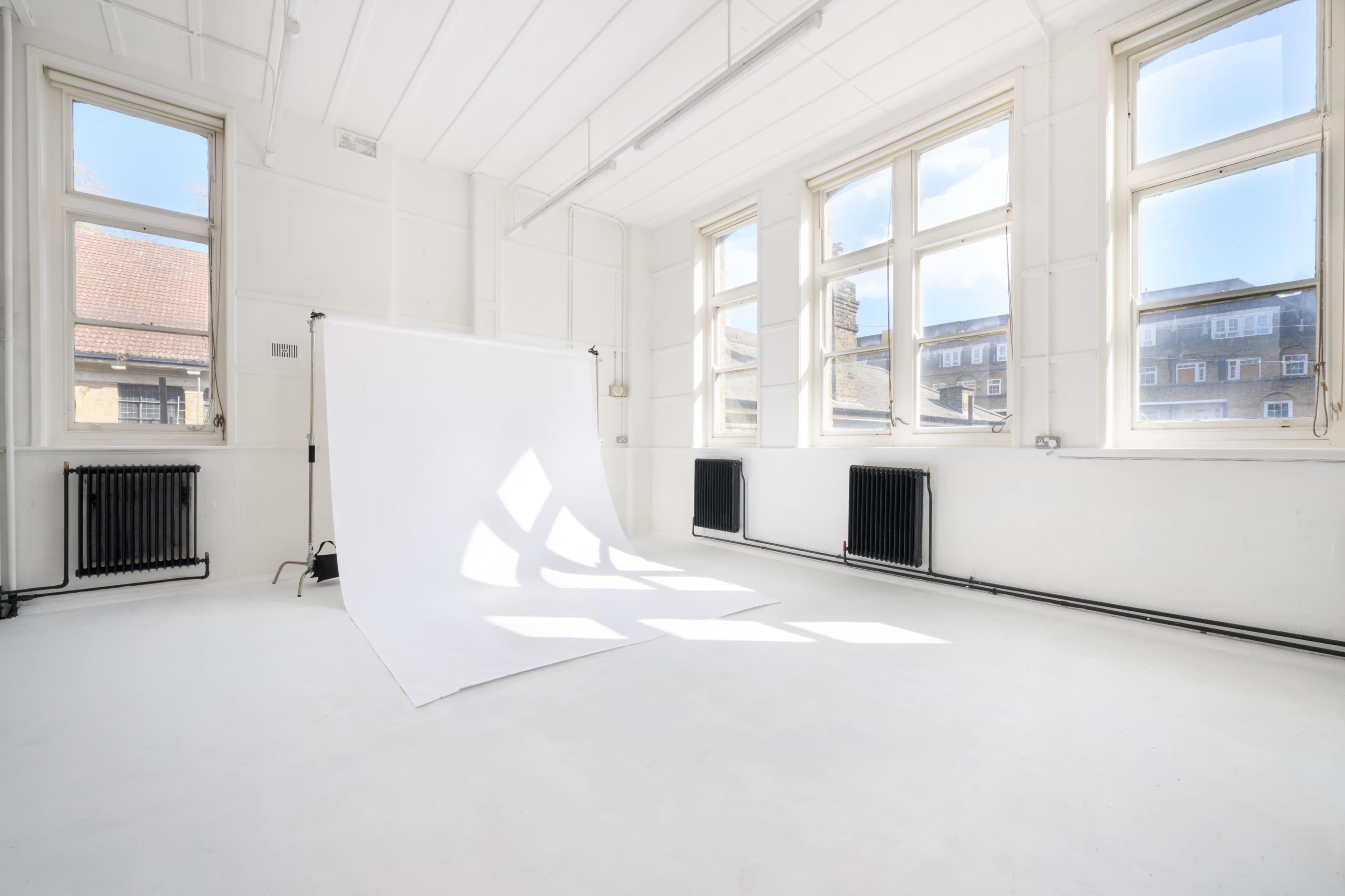 The image shows a bright, empty studio space with large windows, white walls, and a backdrop draped on the floor.