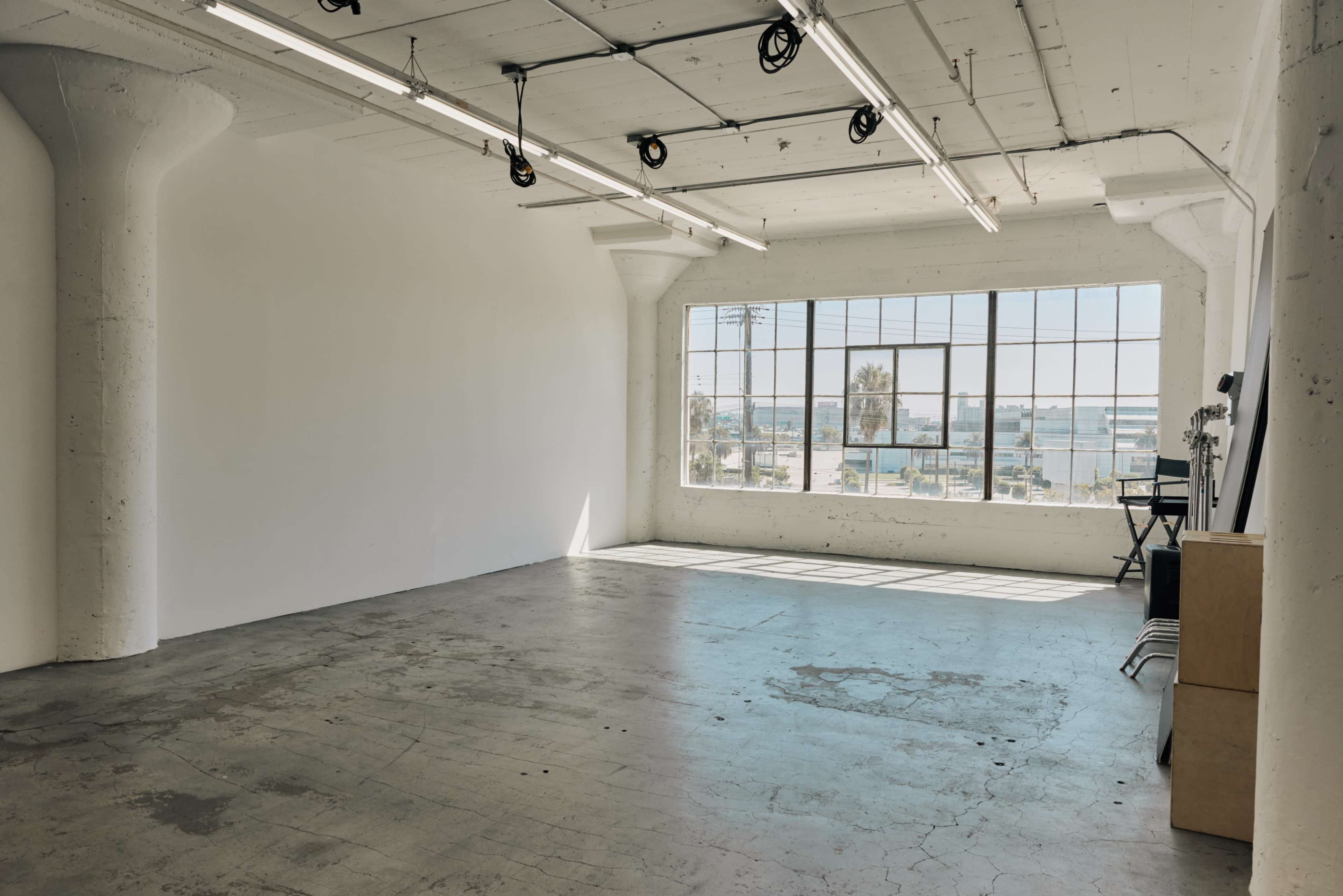 A spacious, empty room with concrete flooring and large windows overlooking a cityscape.