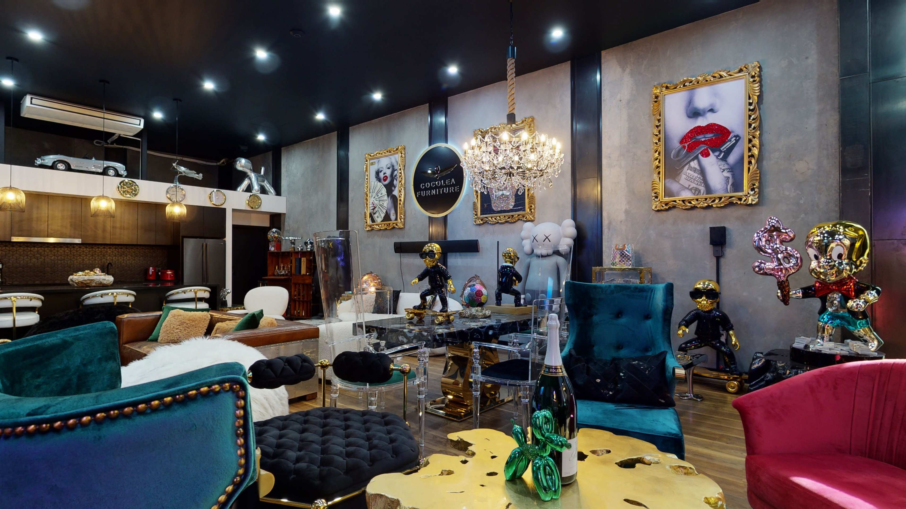 The image shows a stylish interior with colorful furniture, artistic décor, and prominent sculptures displayed against a backdrop of framed artworks.