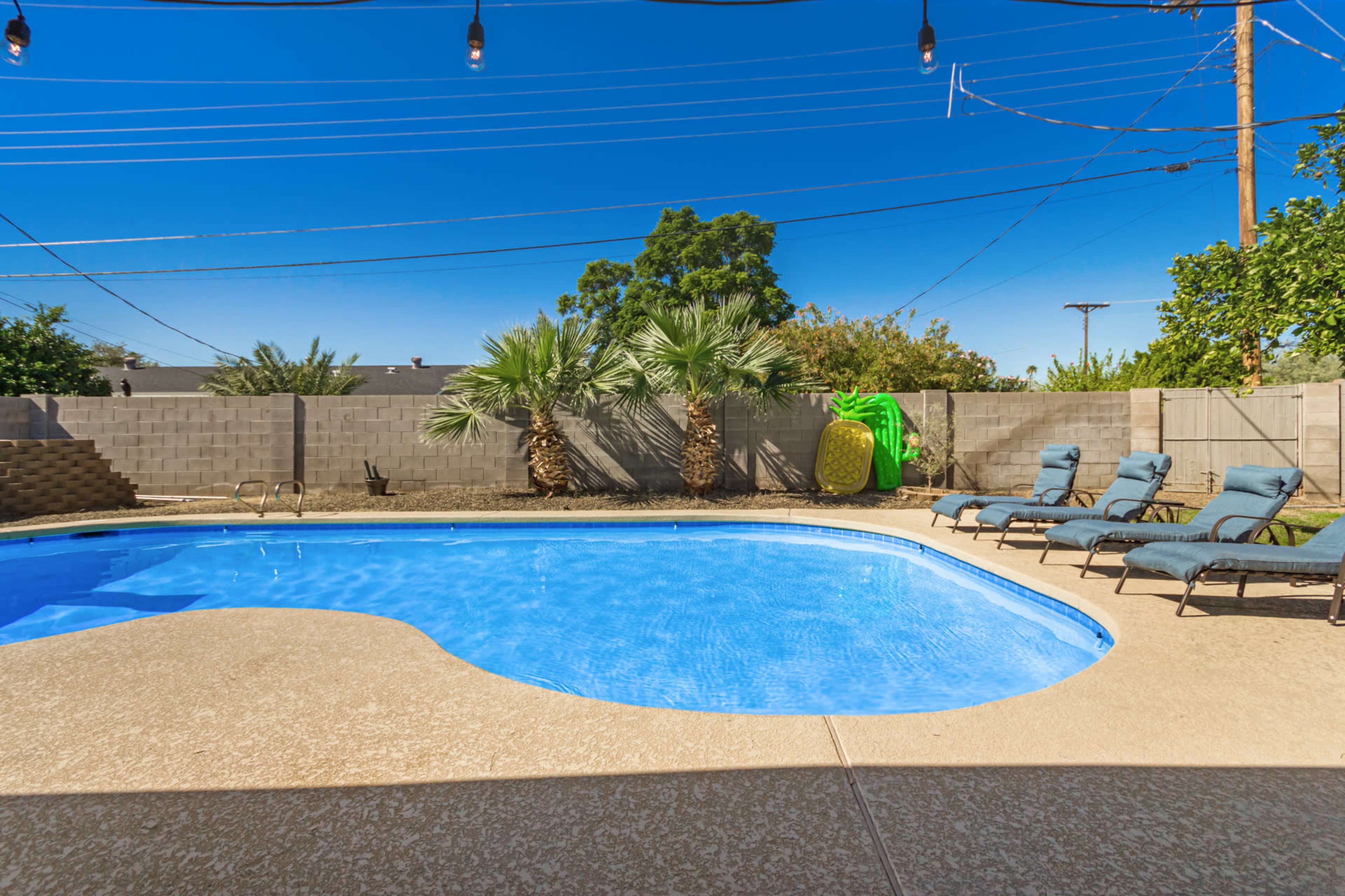 A swimming pool with lounge chairs surrounds it, set against a backdrop of palm trees and a clear blue sky.