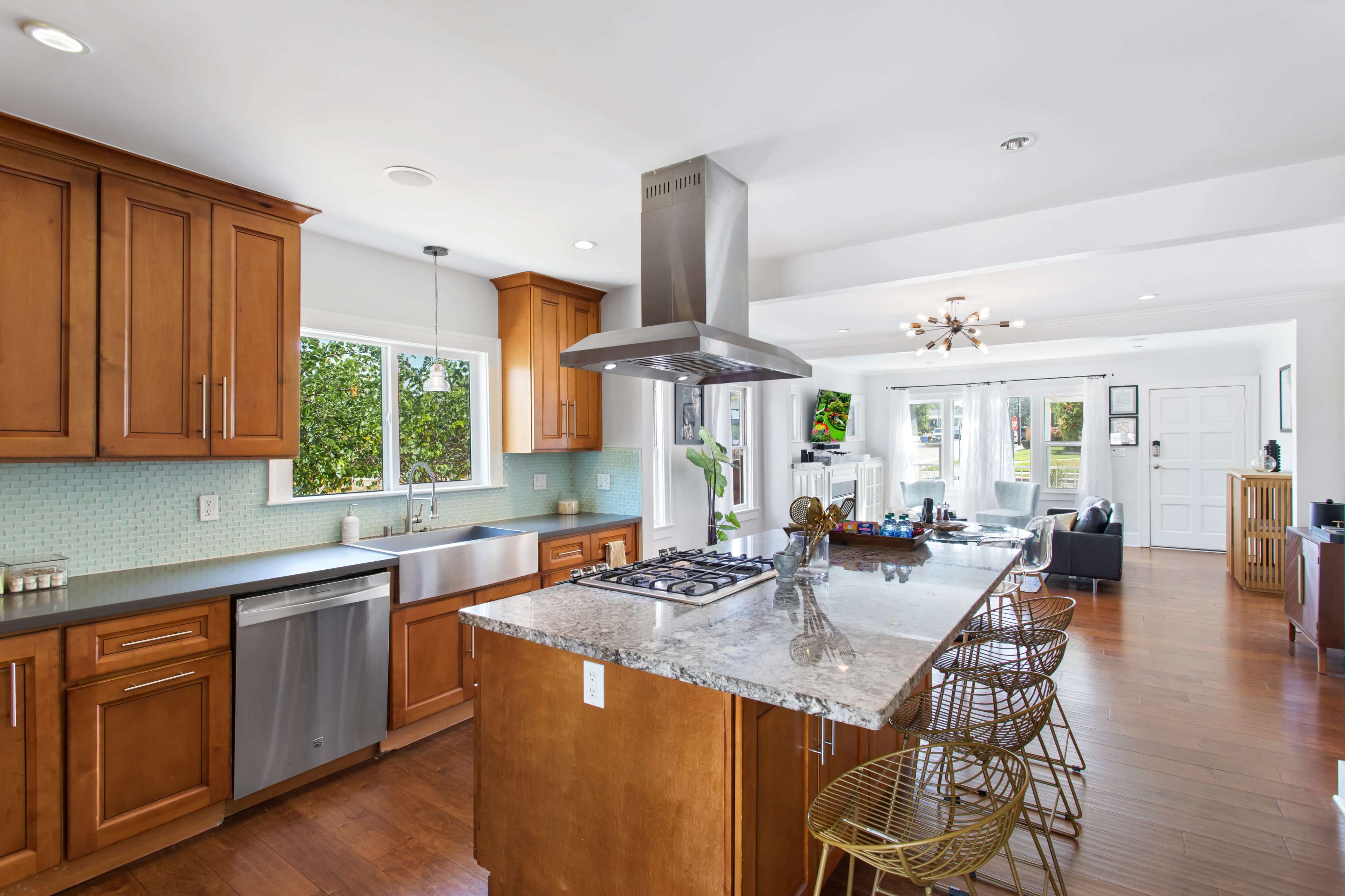 A modern kitchen with wooden cabinets, a large island featuring a gas stove, and stainless steel appliances, along with a dining area visible in the background.