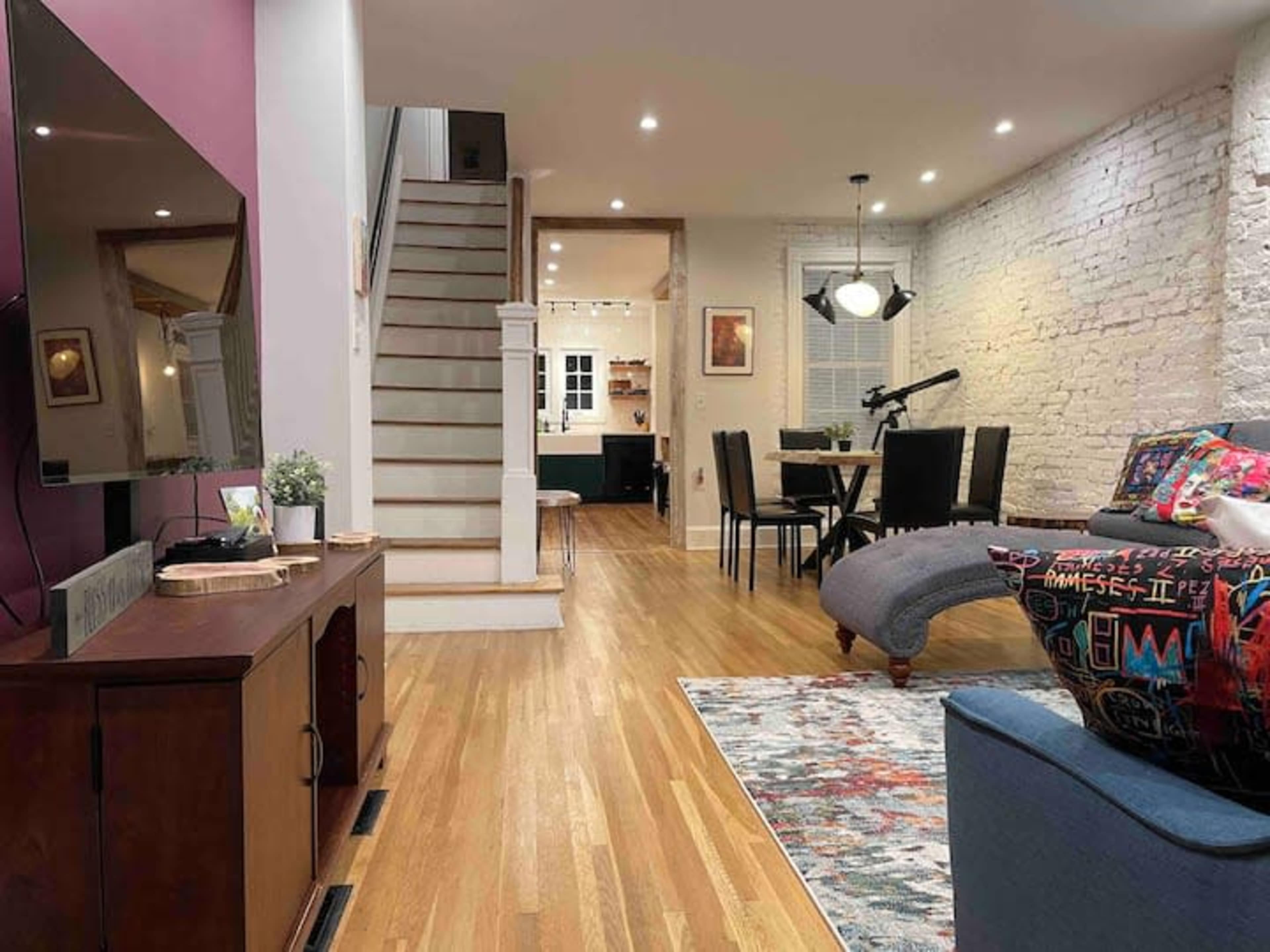 A modern living space with hardwood floors, featuring a staircase, a dining area, and a cozy seating arrangement.