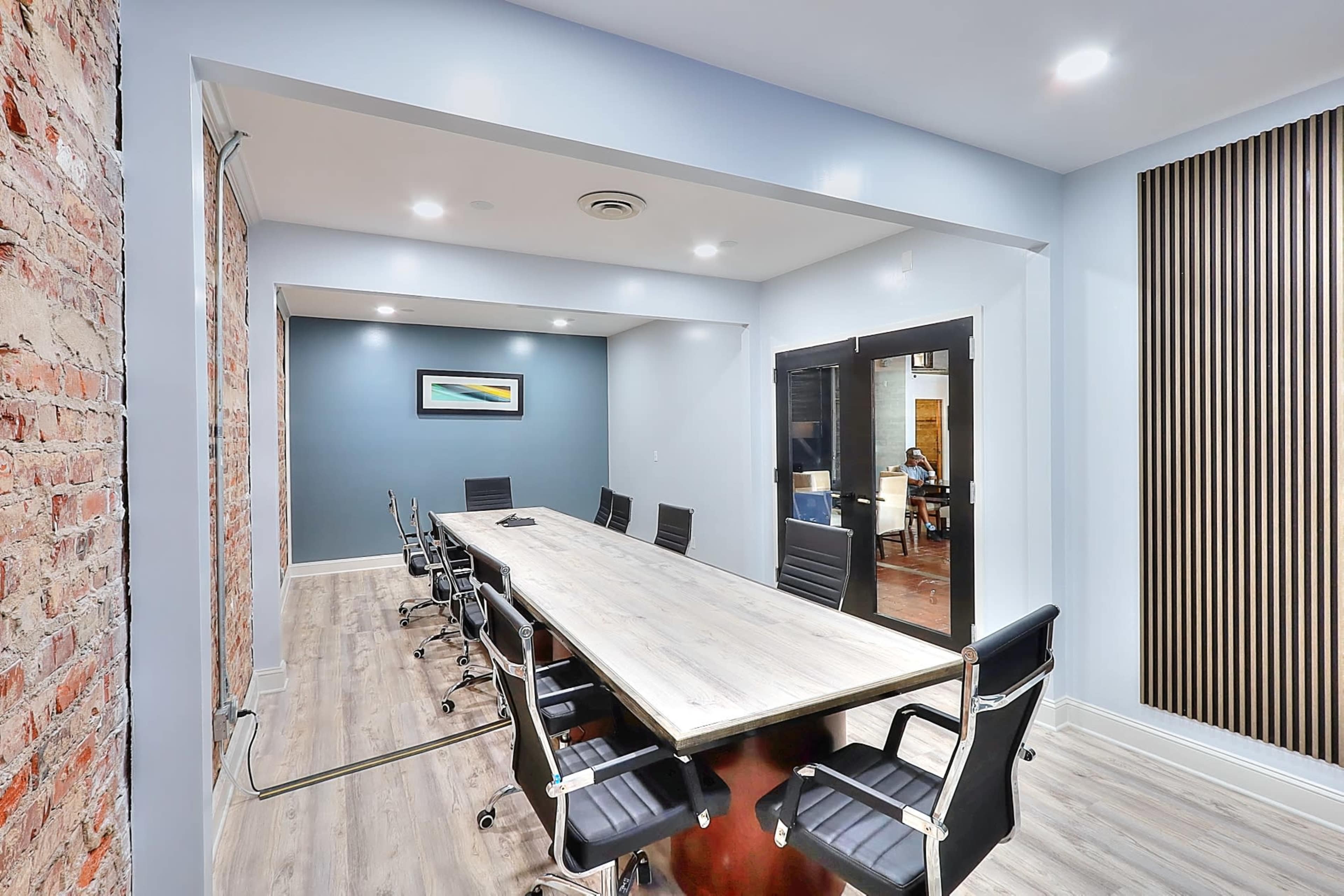 A modern conference room with a long table and black chairs, featuring exposed brick and wooden panel accents on the walls.