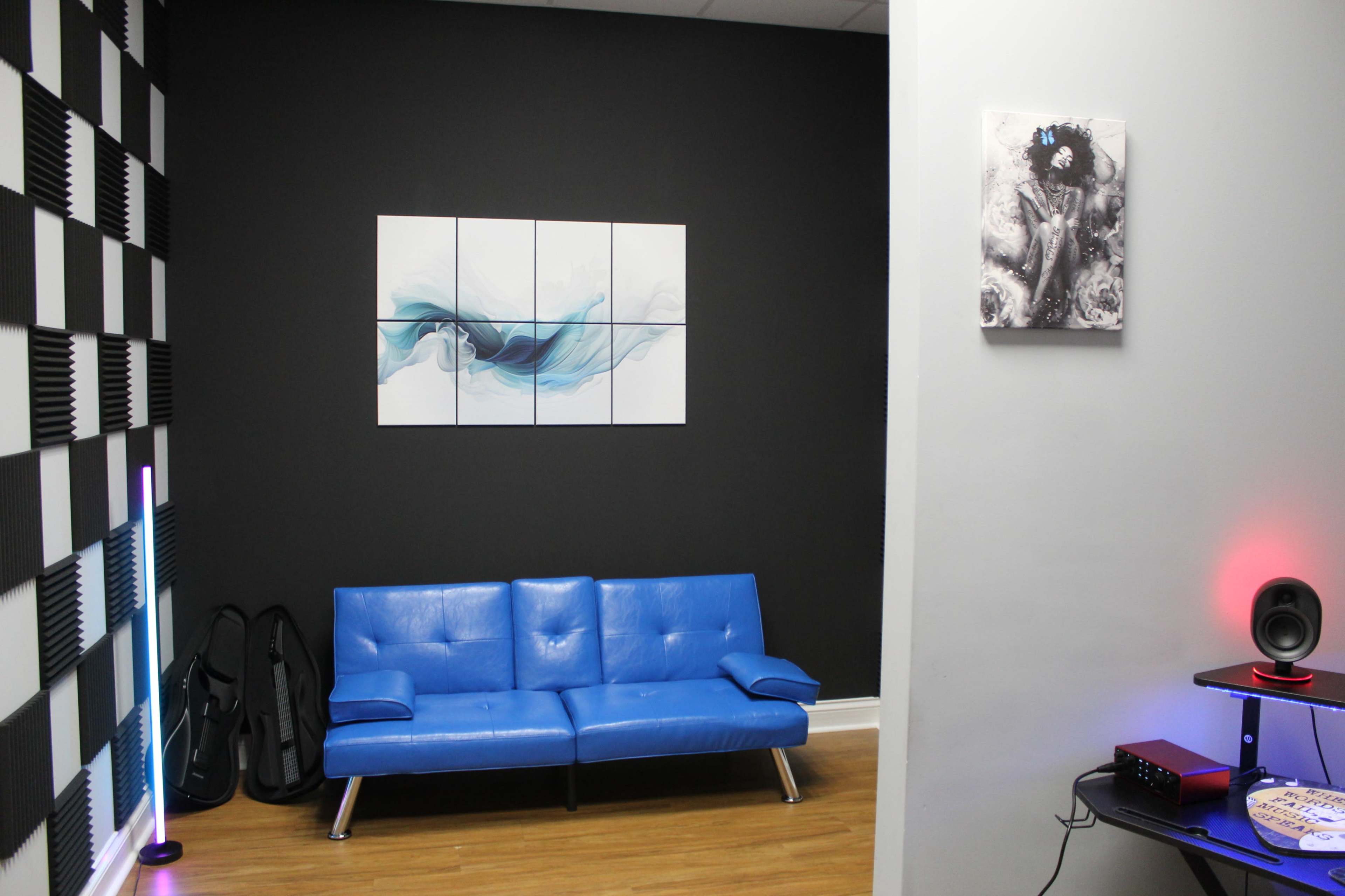 The image shows a room with a blue sofa, abstract wall art, and a checkered wall opposite, featuring speakers and a music setup.