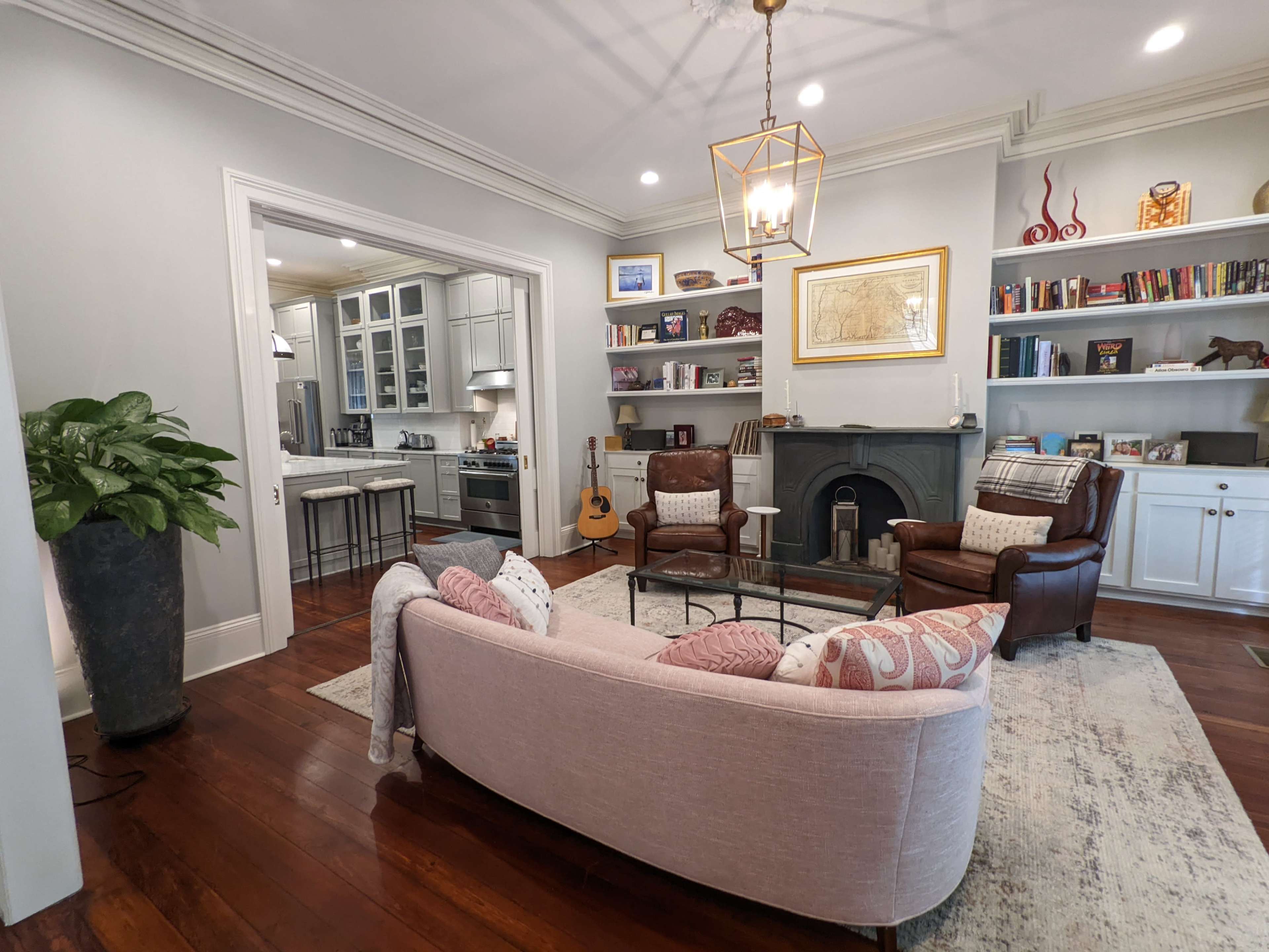 A living room with two chairs and a sofa, a fireplace, built-in bookshelves, a guitar, and a large potted plant.