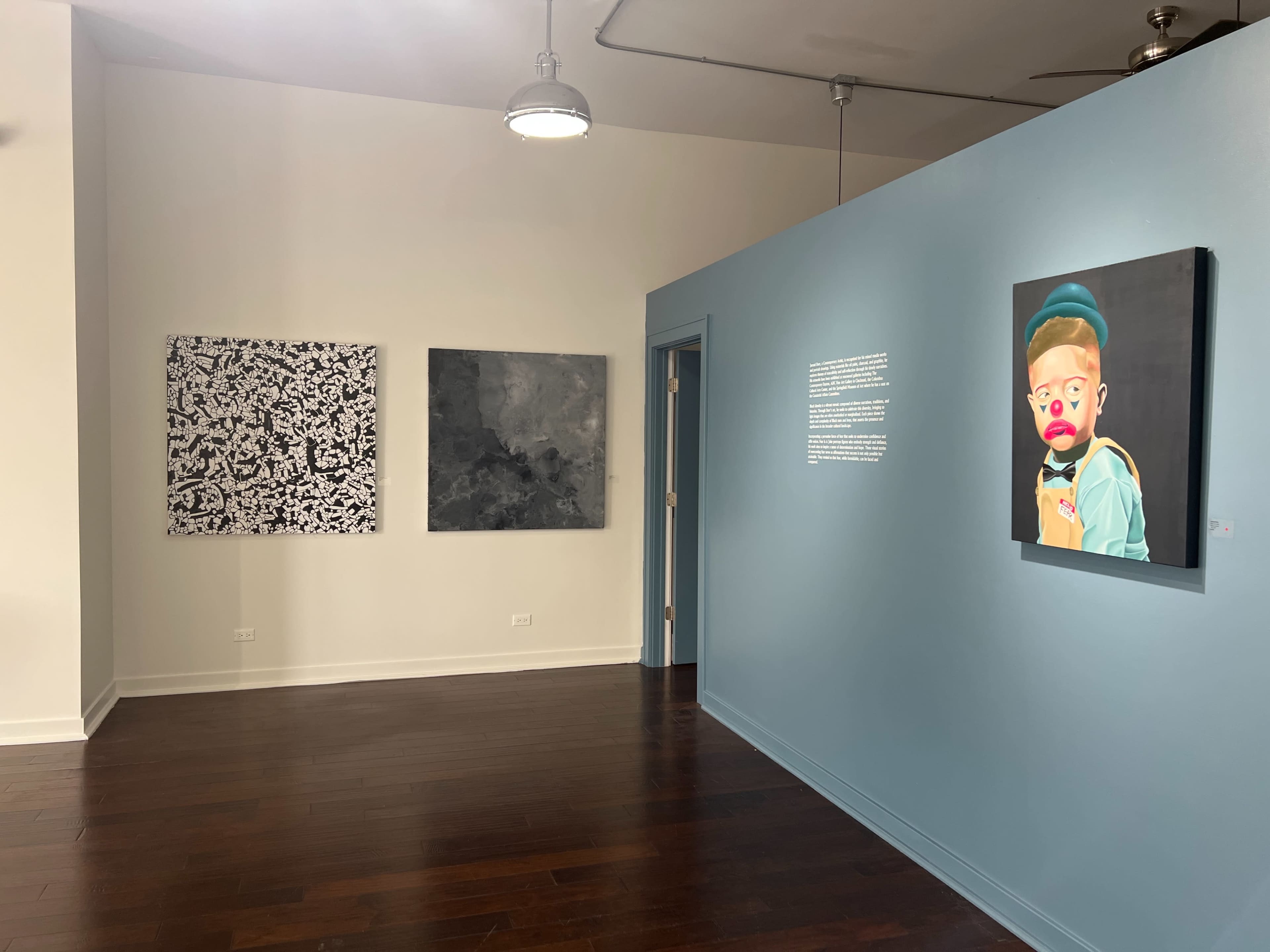An art gallery with three paintings on the wall and a blue wall featuring a portrait on the right side.