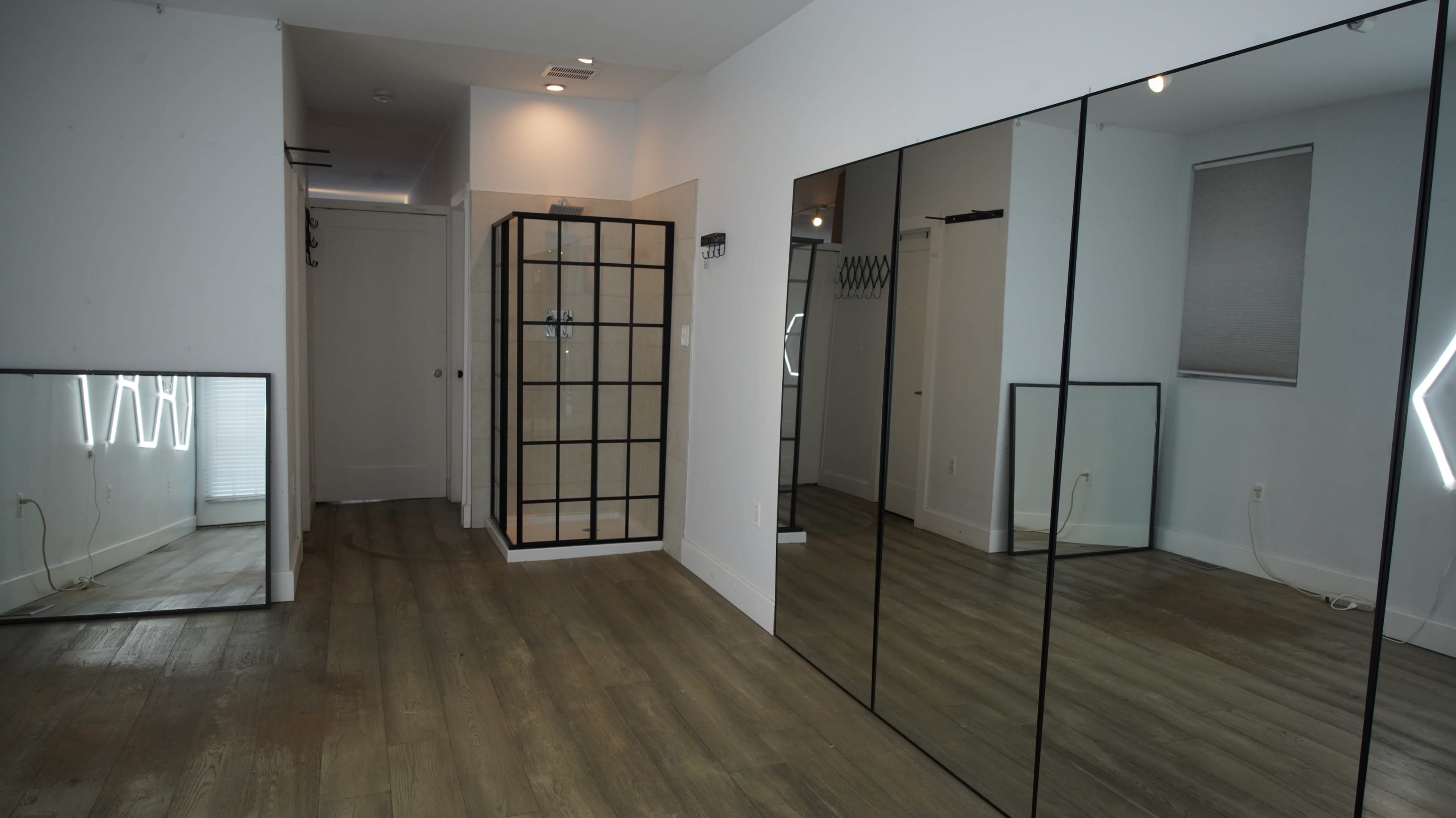 The image shows a spacious room featuring large mirrors on one wall, a glass-block shower enclosure, and light wood flooring.