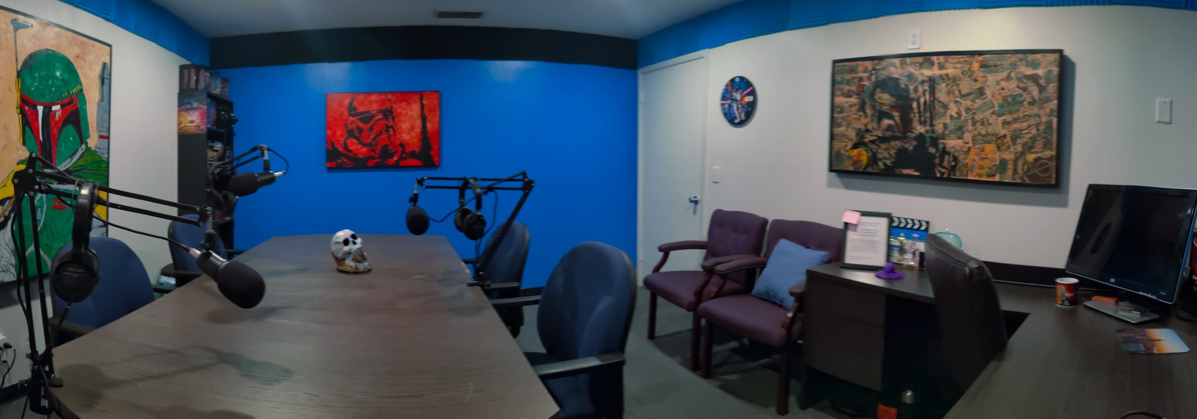 A small meeting room with a long table, several chairs, microphones, and artwork on the blue walls.