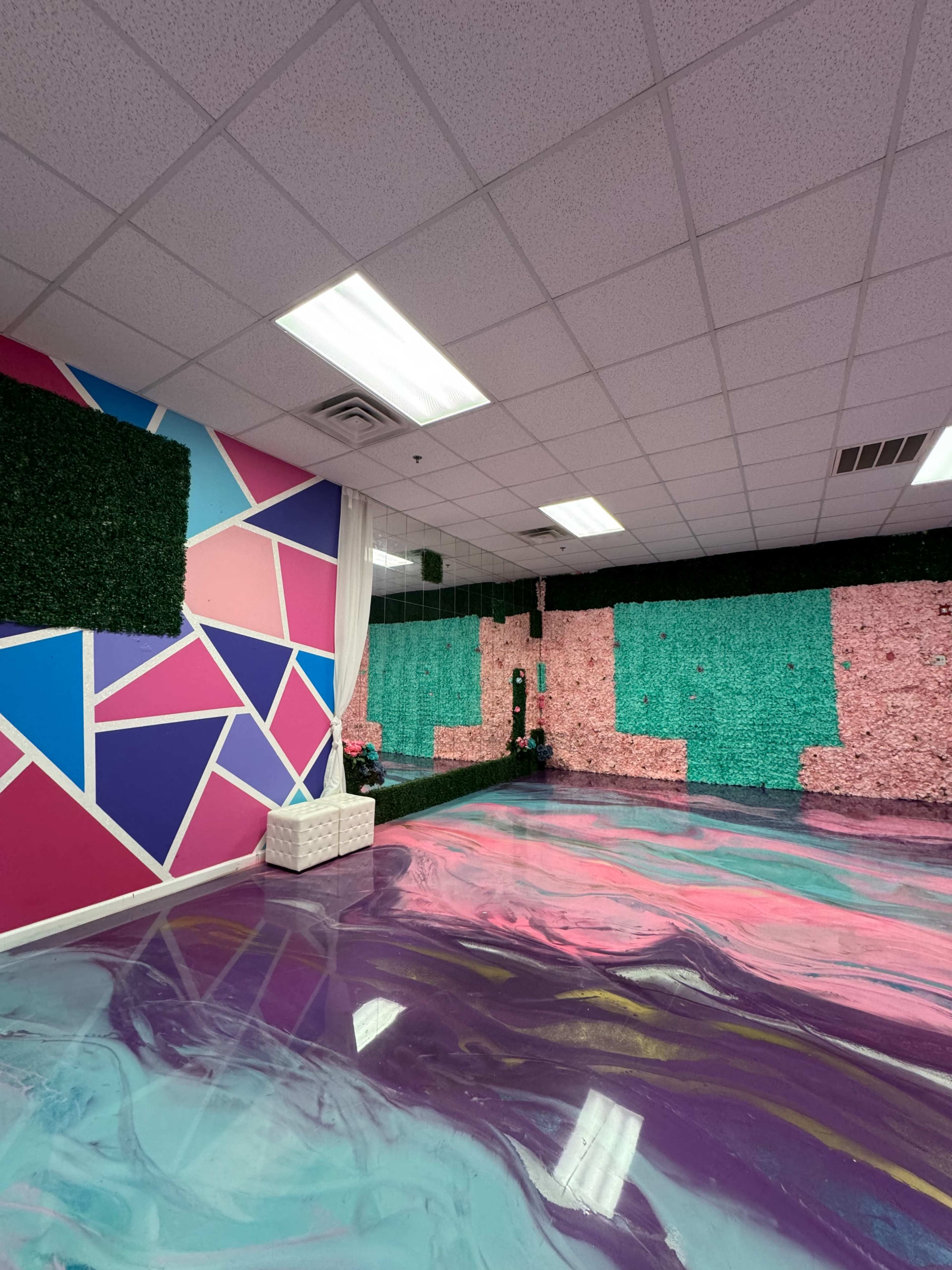 A vibrant indoor space featuring a multi-colored geometric wall design, a textured green wall, and a smooth purple and pink patterned floor.
