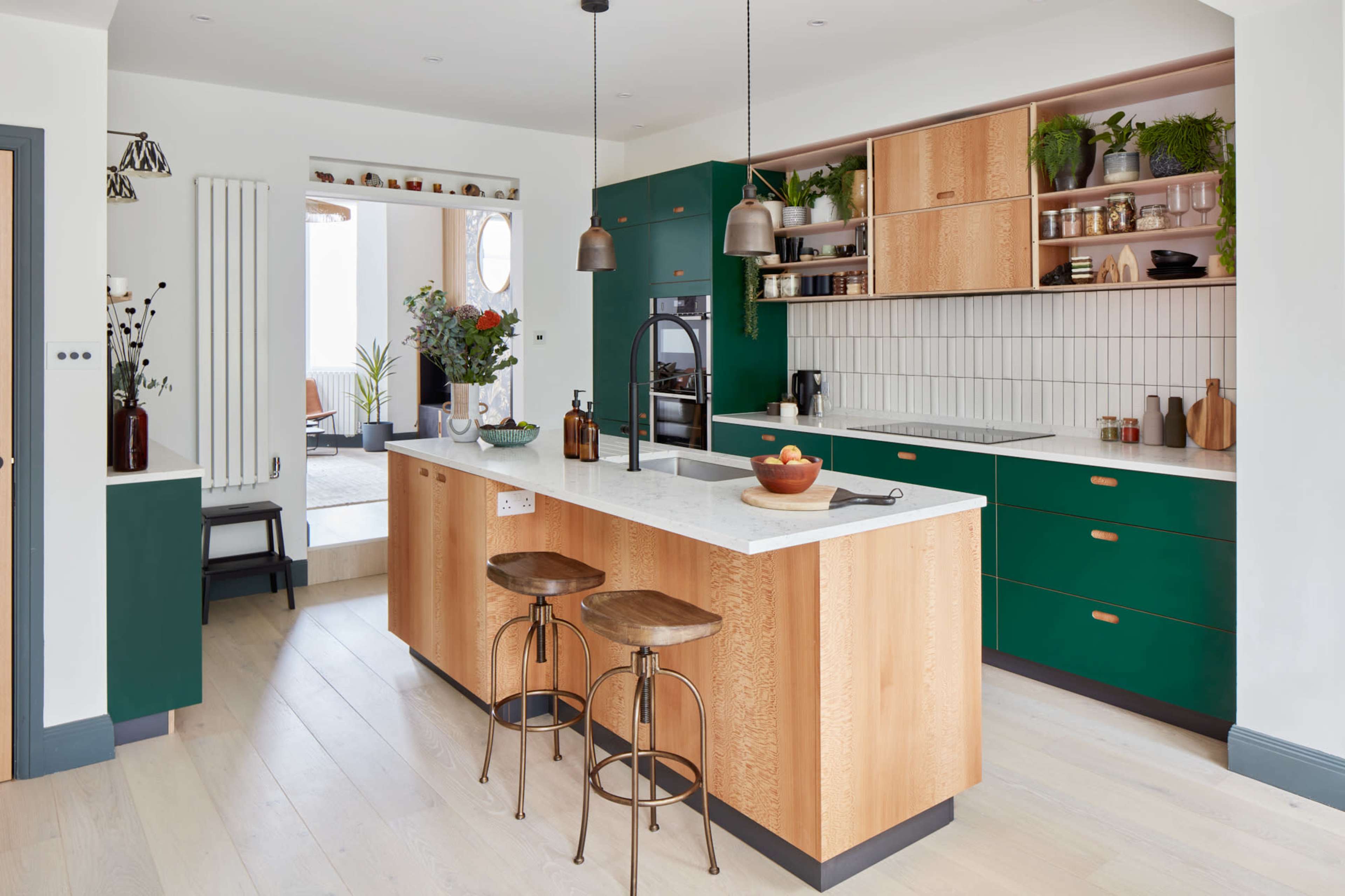 A modern kitchen featuring a central island with wooden stools, green cabinetry, and a marble countertop.