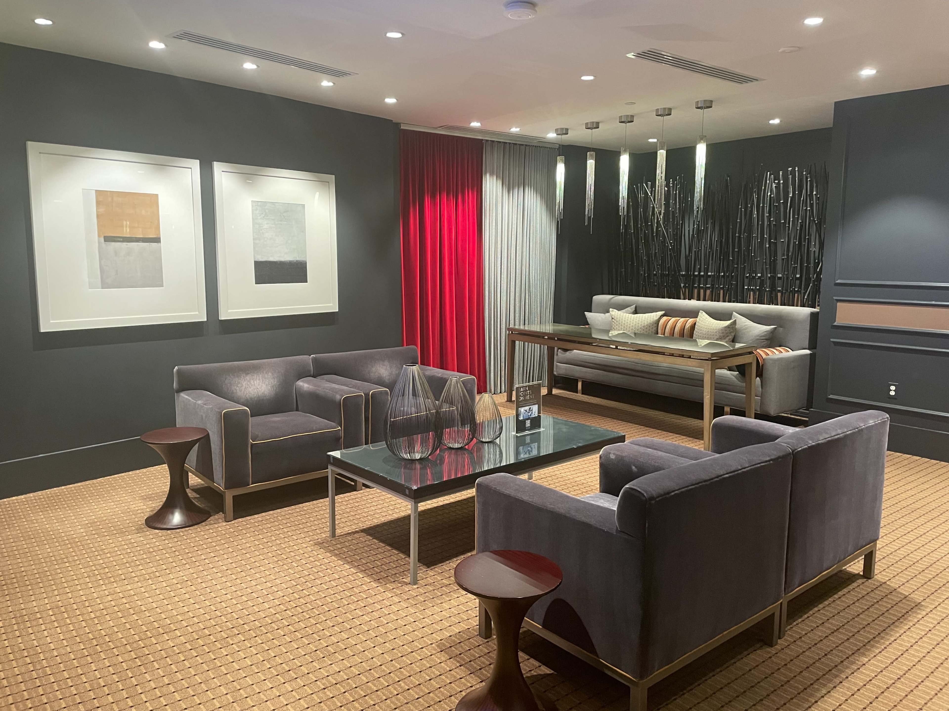 A stylish lounge area featuring gray sofas, a glass coffee table, and artwork on the walls, illuminated by soft overhead lighting.