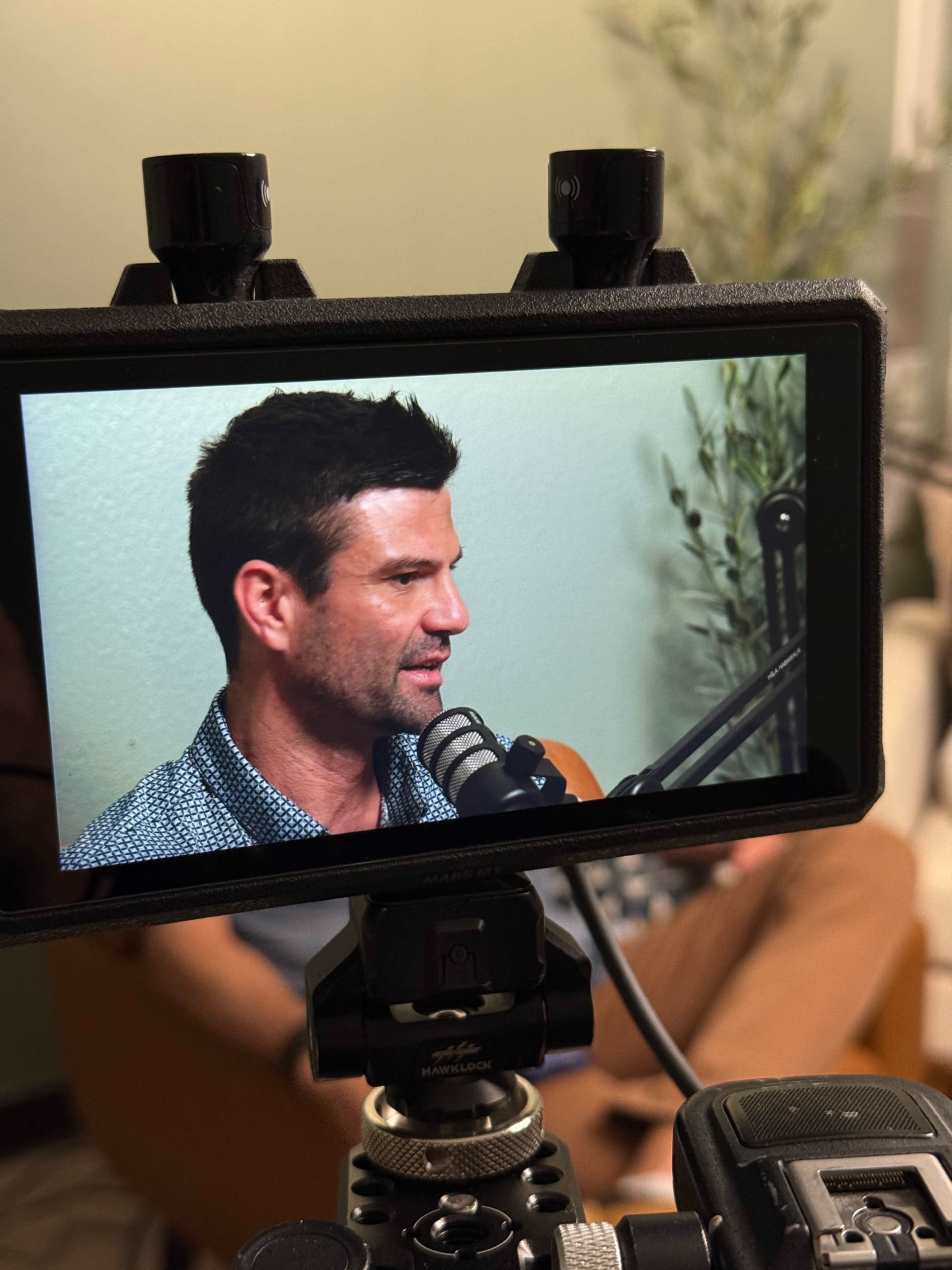 A man sitting in a chair is being recorded on a camera with a microphone positioned in front of him.