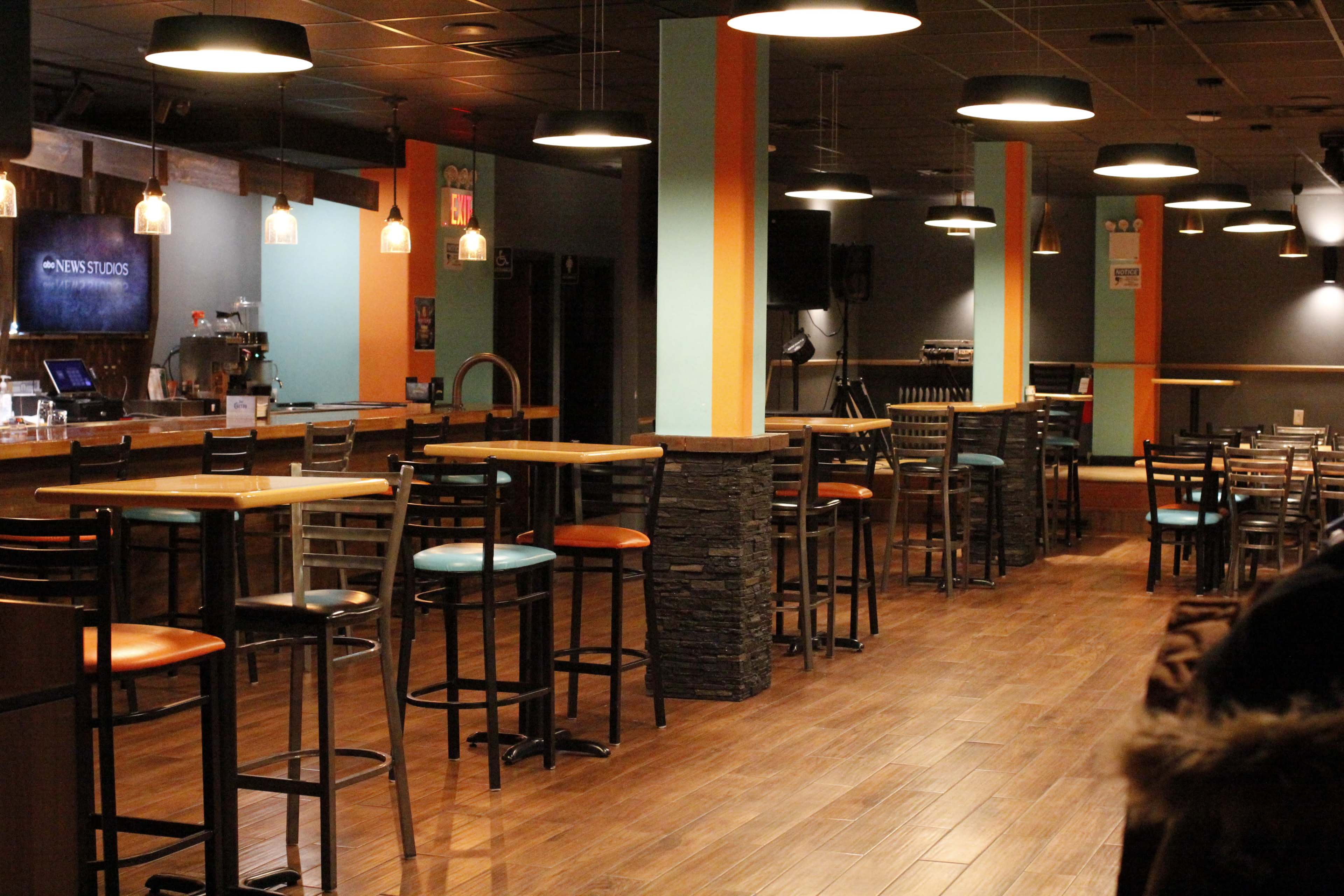 An empty bar area featuring high tables and stools, with a wooden counter and soft lighting.