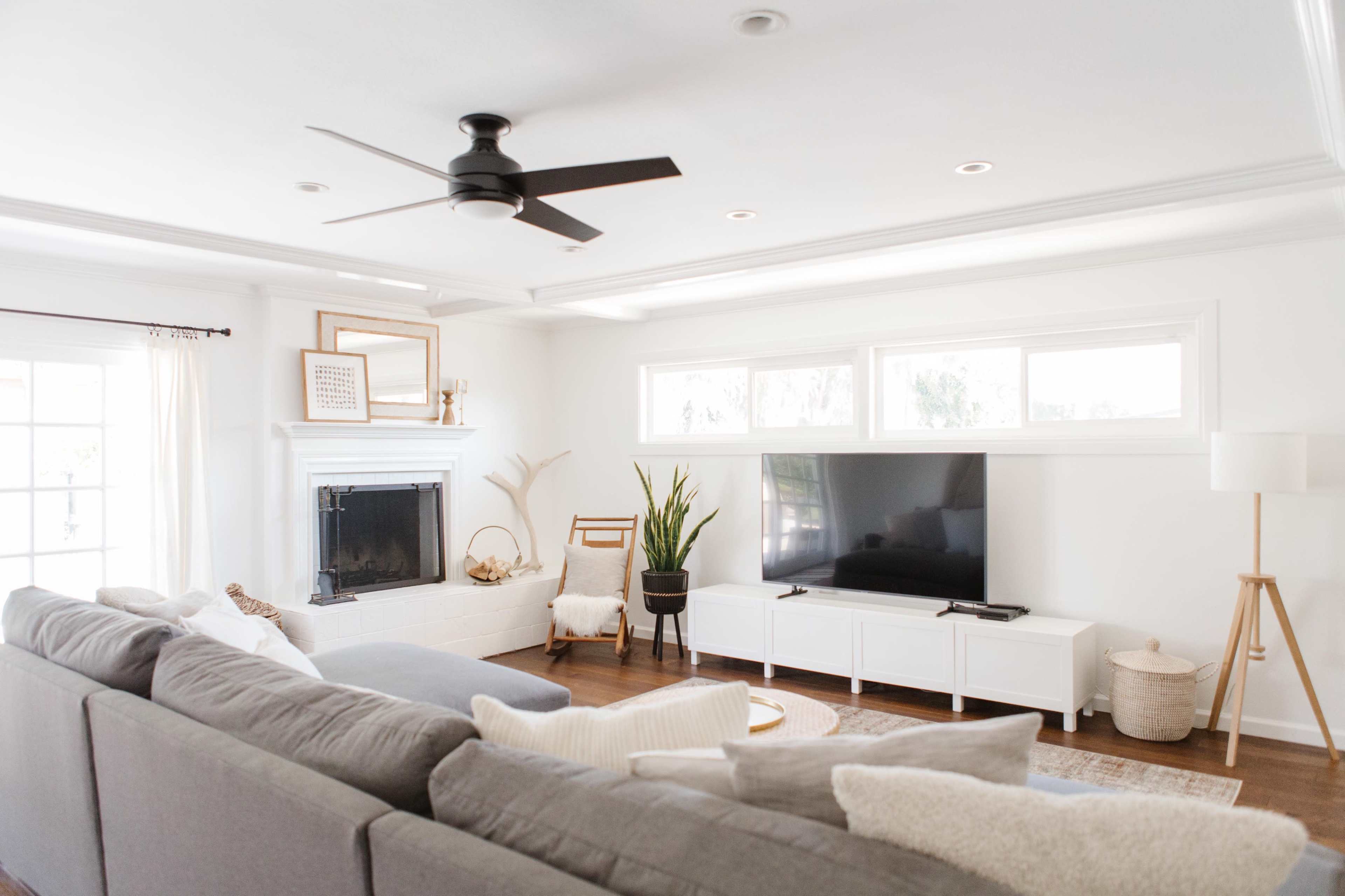 A modern living room features a gray sectional sofa, a large flat-screen TV on a white media console, and a fireplace with decorative elements.