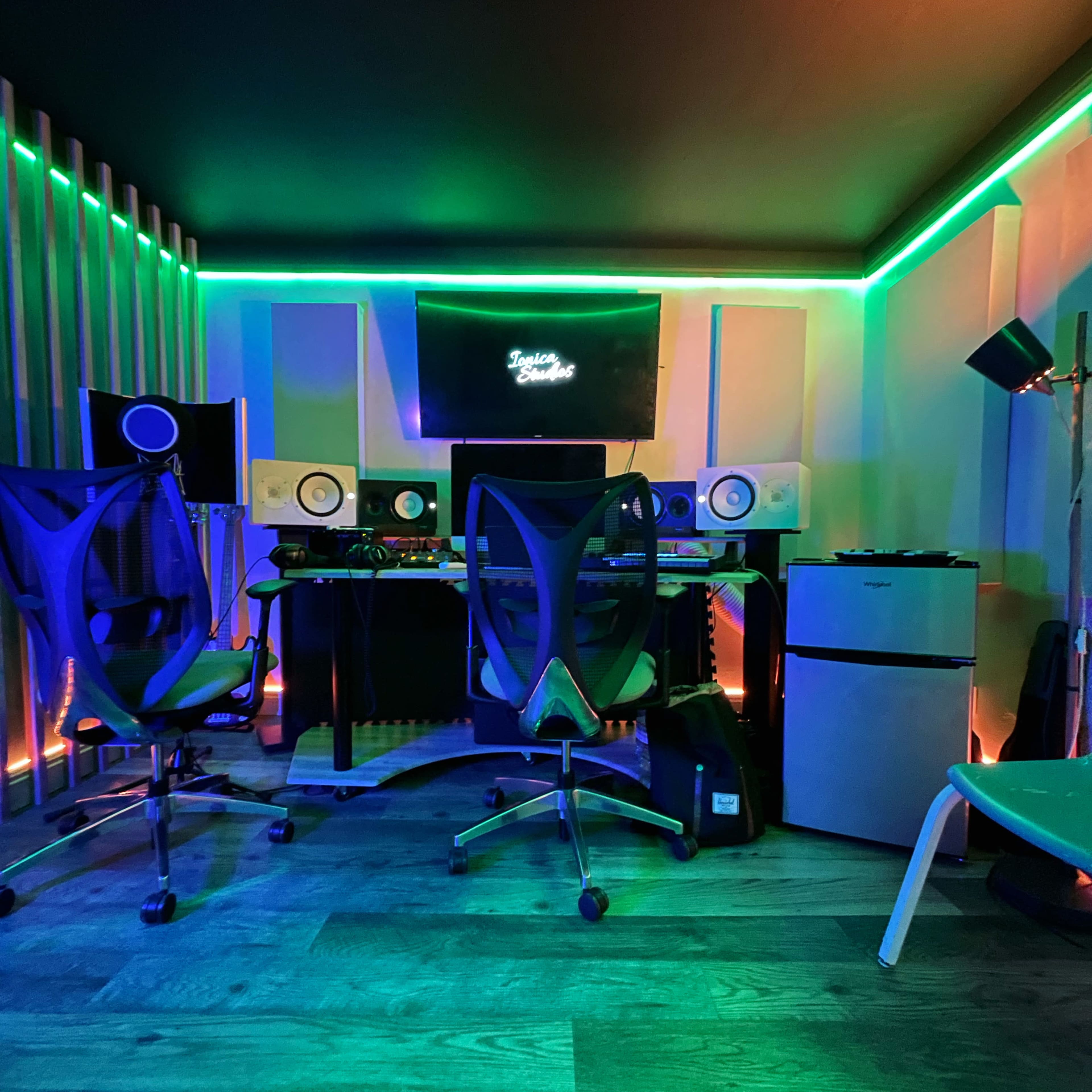 A modern music production studio featuring a computer setup, studio monitors, and colorful LED lighting.