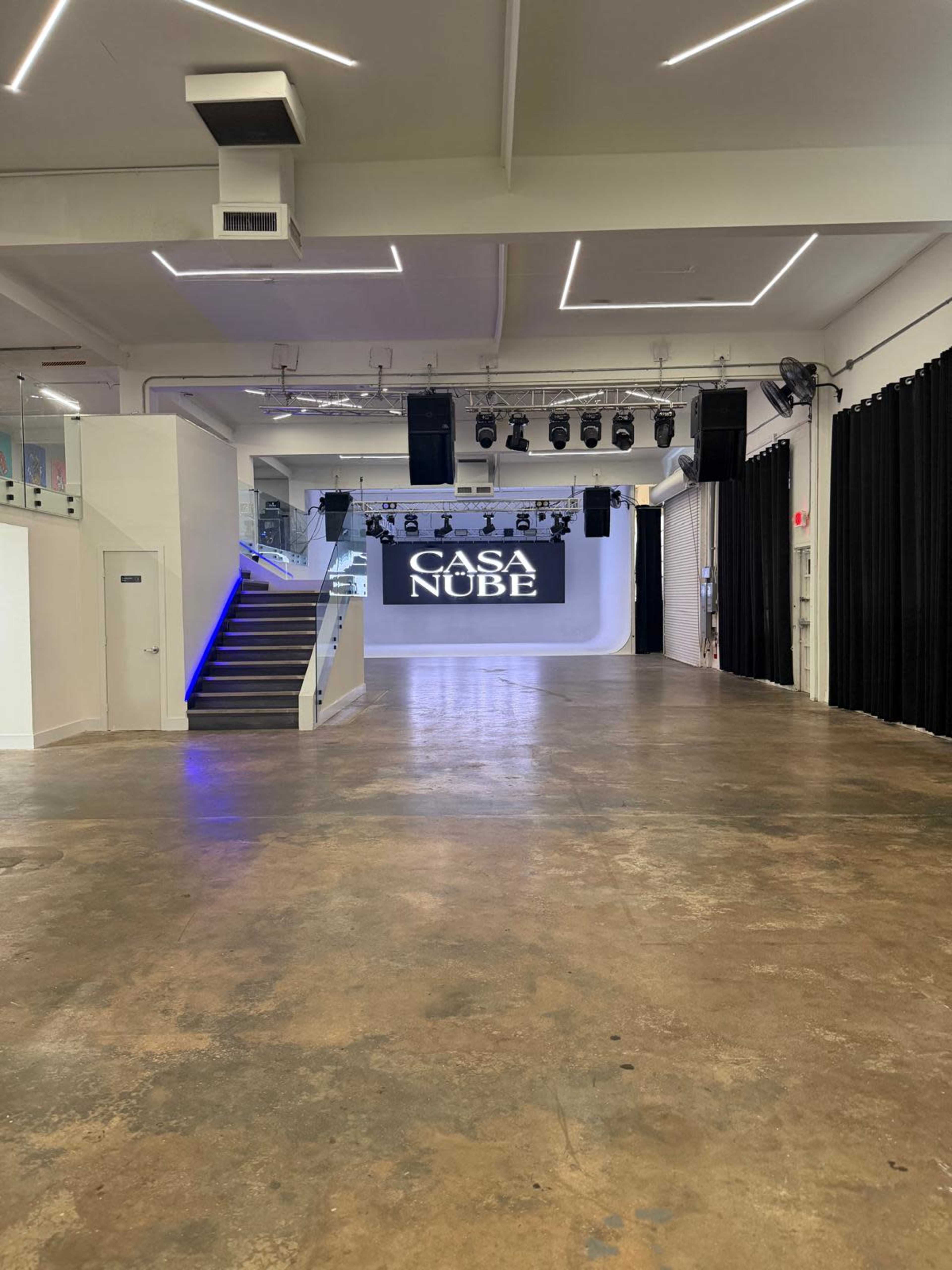 The image shows an empty event space featuring a large screen with the text "CASA NUBE" and modern lighting.