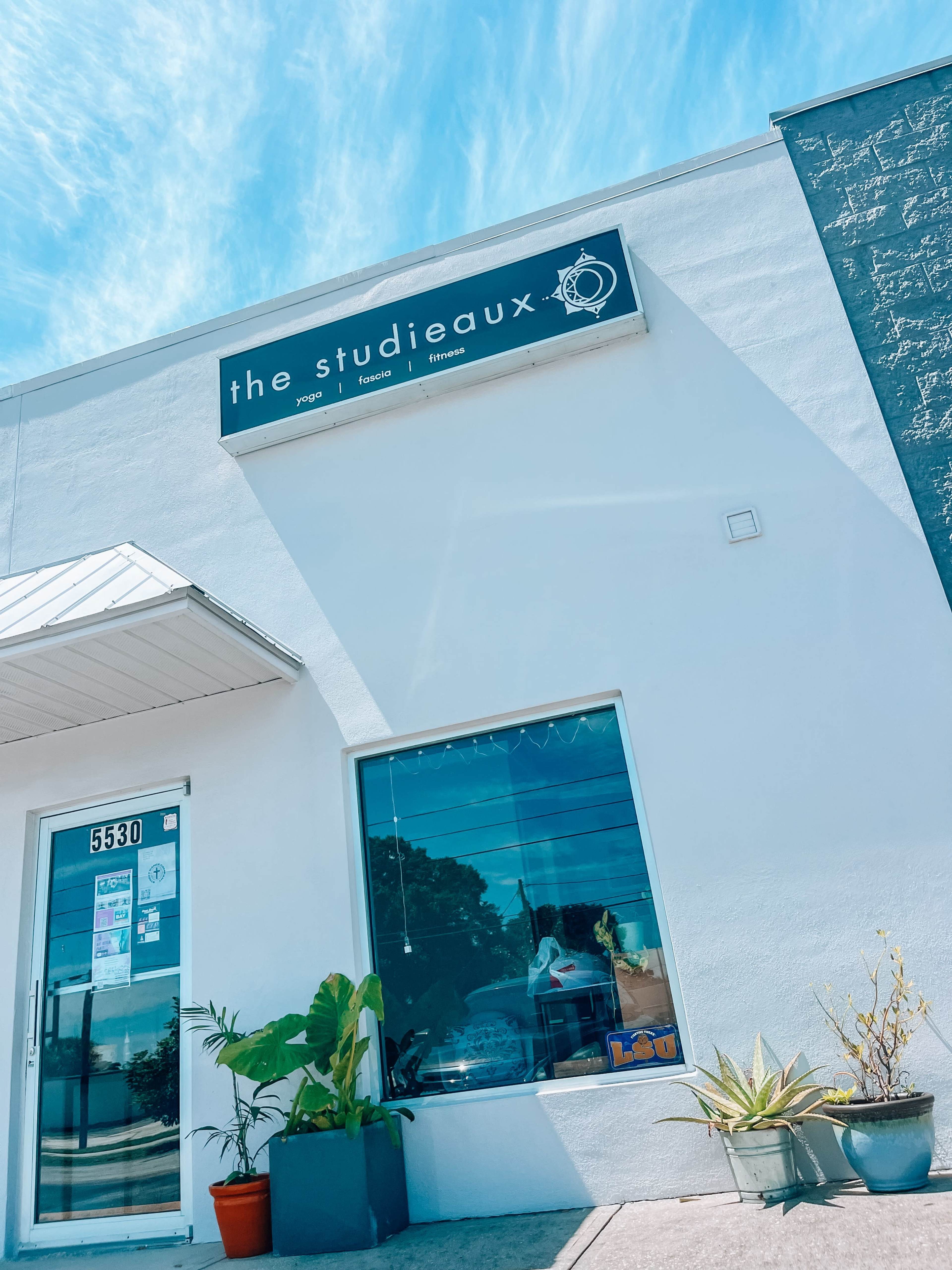 The image shows a white building with a sign that reads "the studieaux" above a large window, which displays plants and a view of the street.