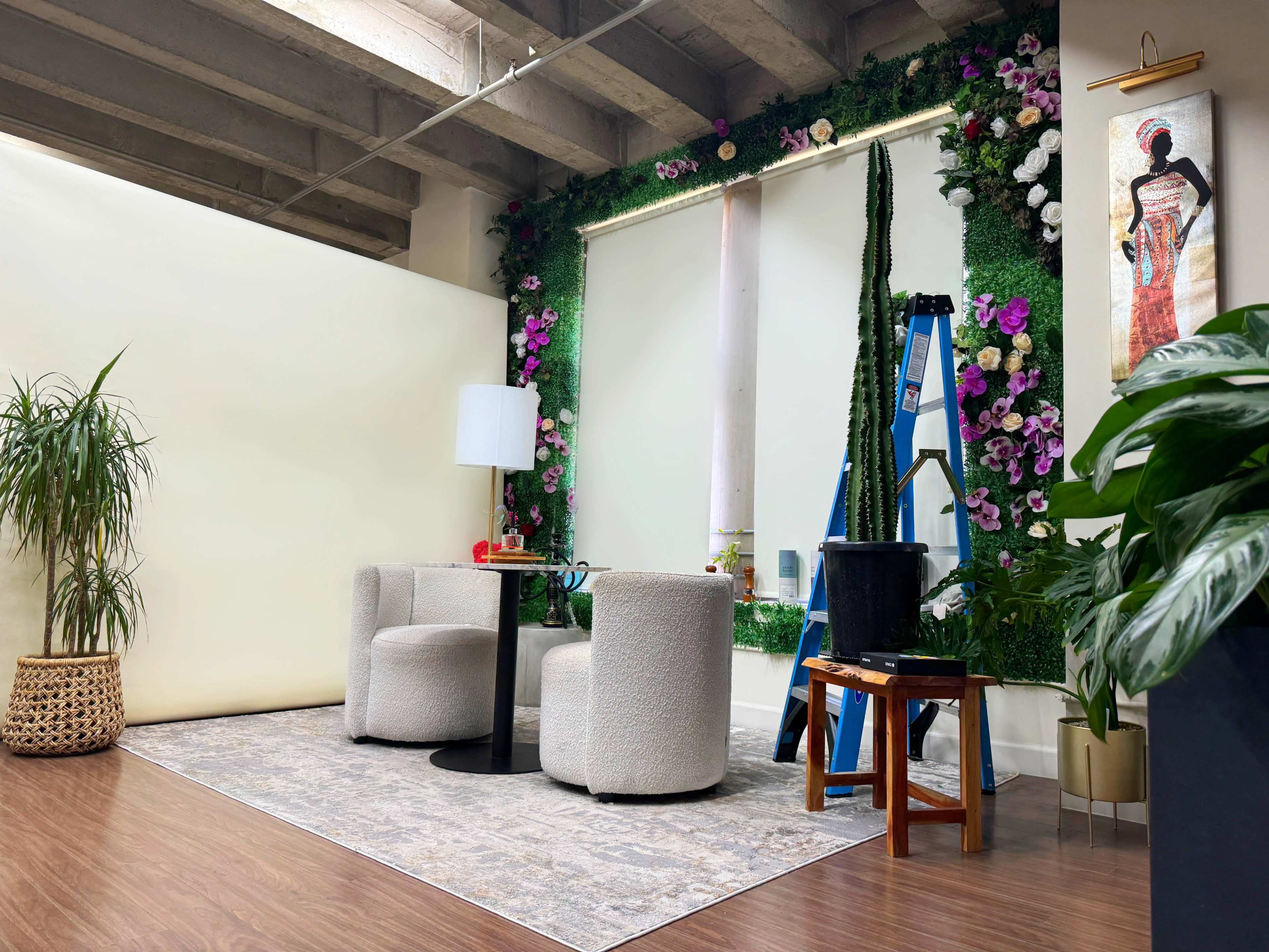 The scene features a cozy indoor setup with two round chairs and a small table, surrounded by a decorative floral wall and a ladder nearby.
