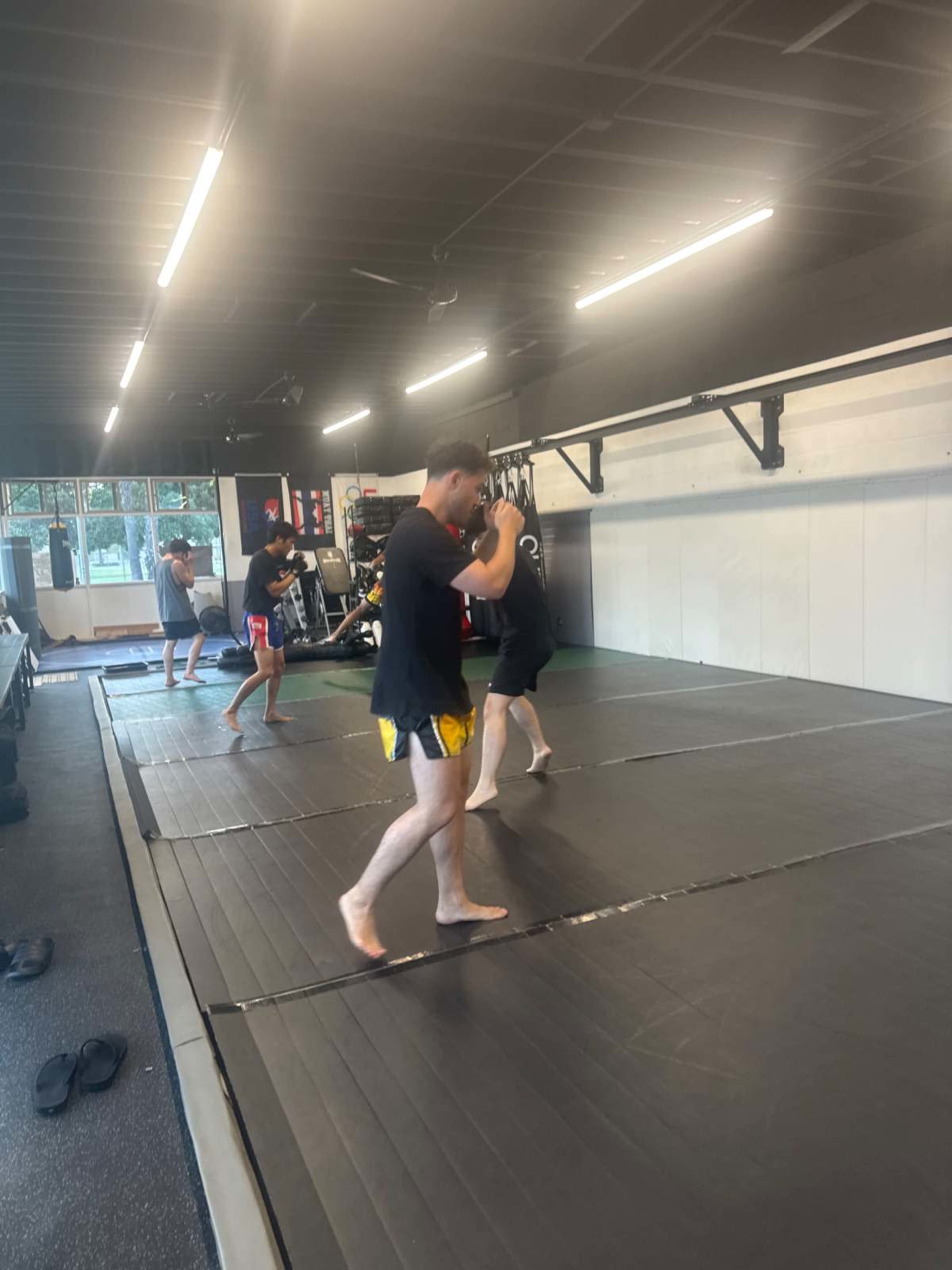 Four individuals practice striking techniques on a padded training mat in a gym setting.